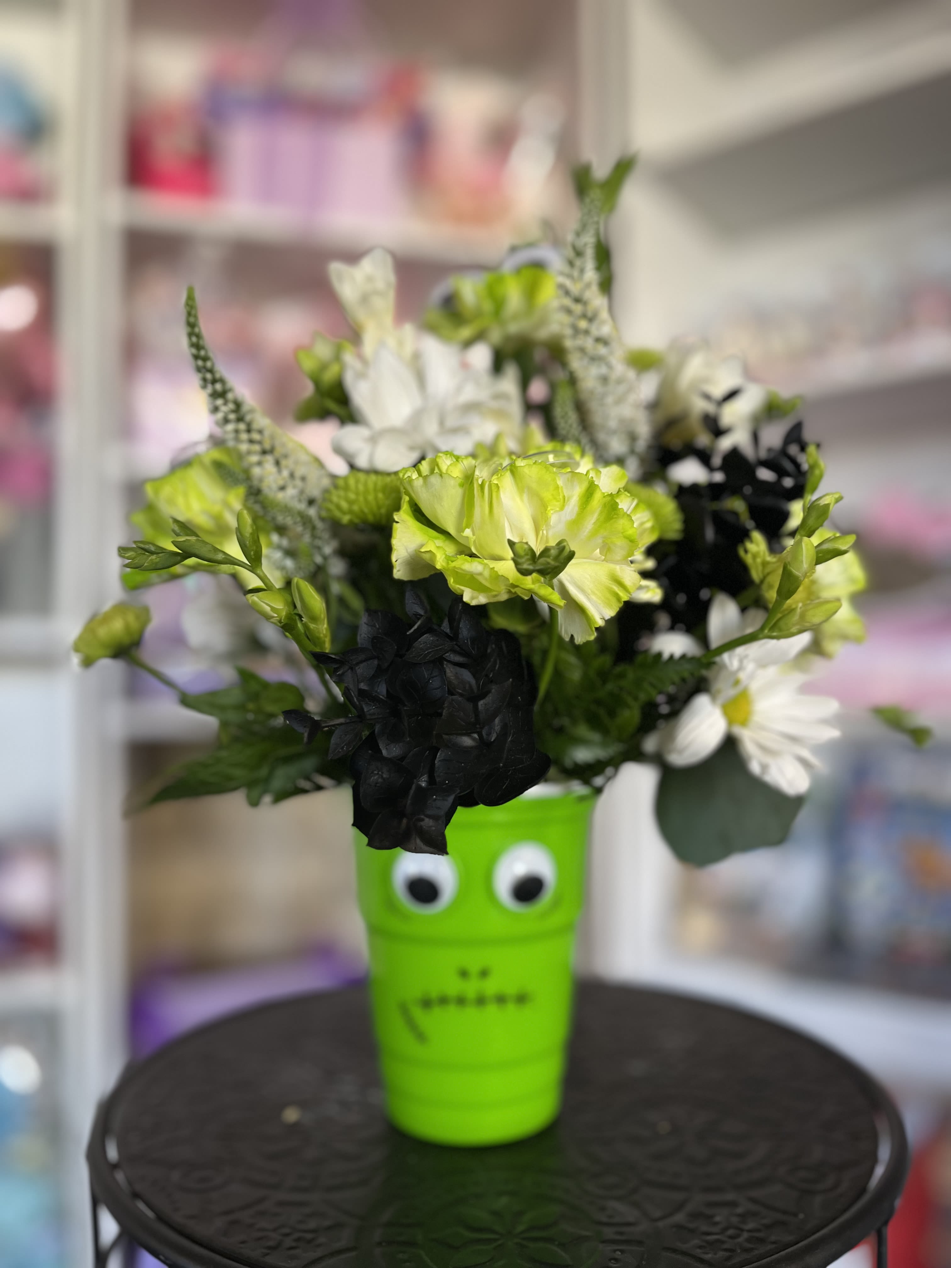 Bouquet of green, white, and black flowers in a bright green cup with eyes