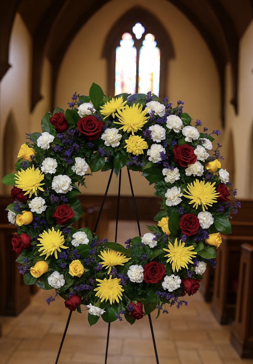Circular funeral wreath of red, yellow, and white flowers on an easel