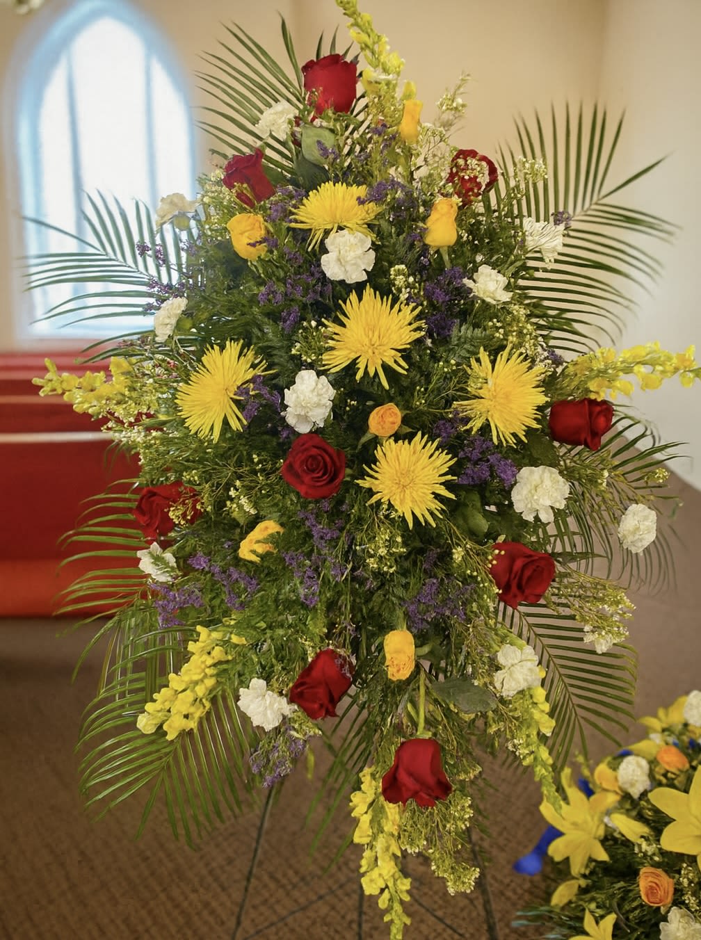 Tall funeral spray with red roses, yellow spider mums, and white carnations