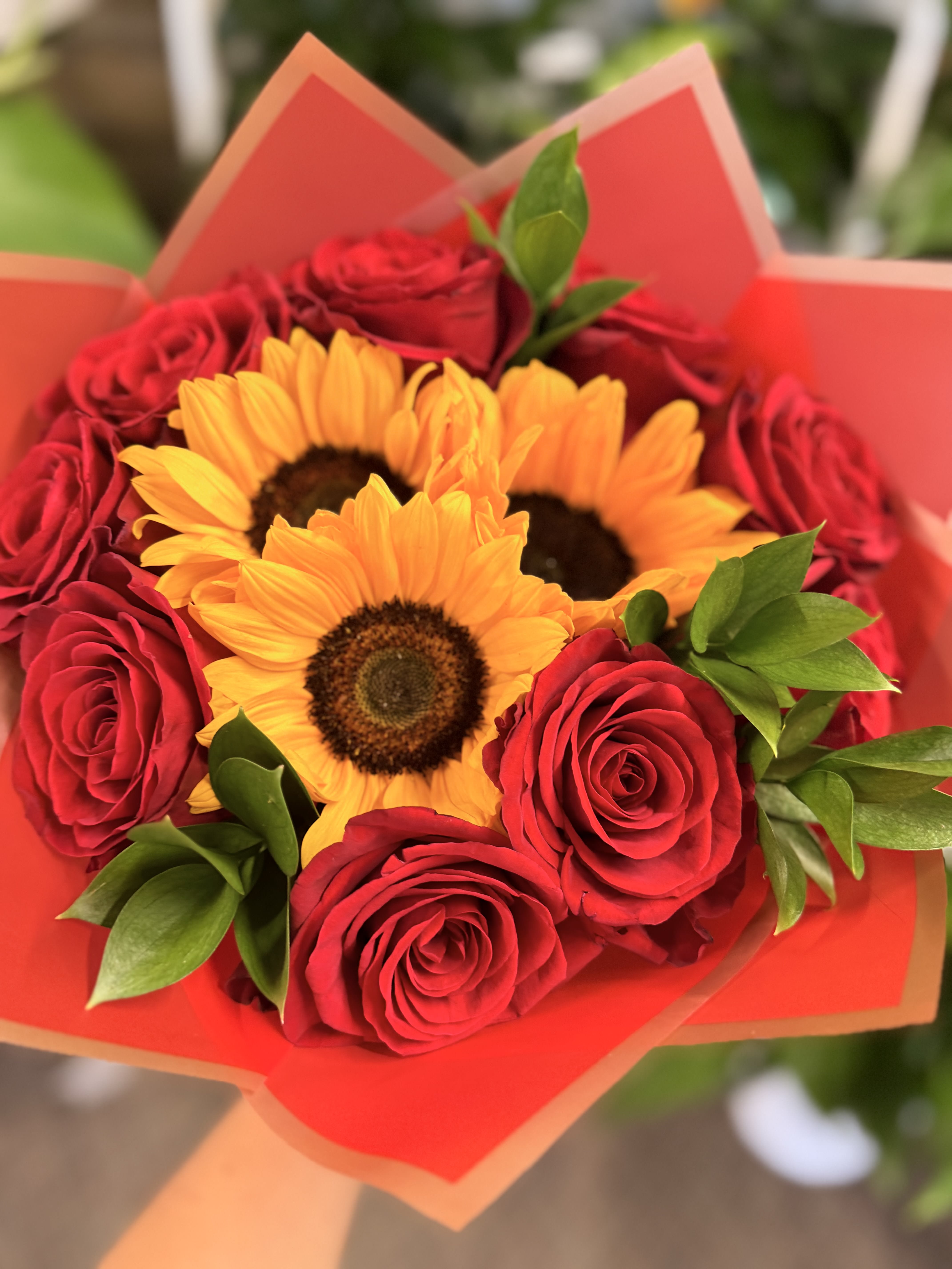 Bouquet of red roses and yellow sunflowers wrapped in orange paper
