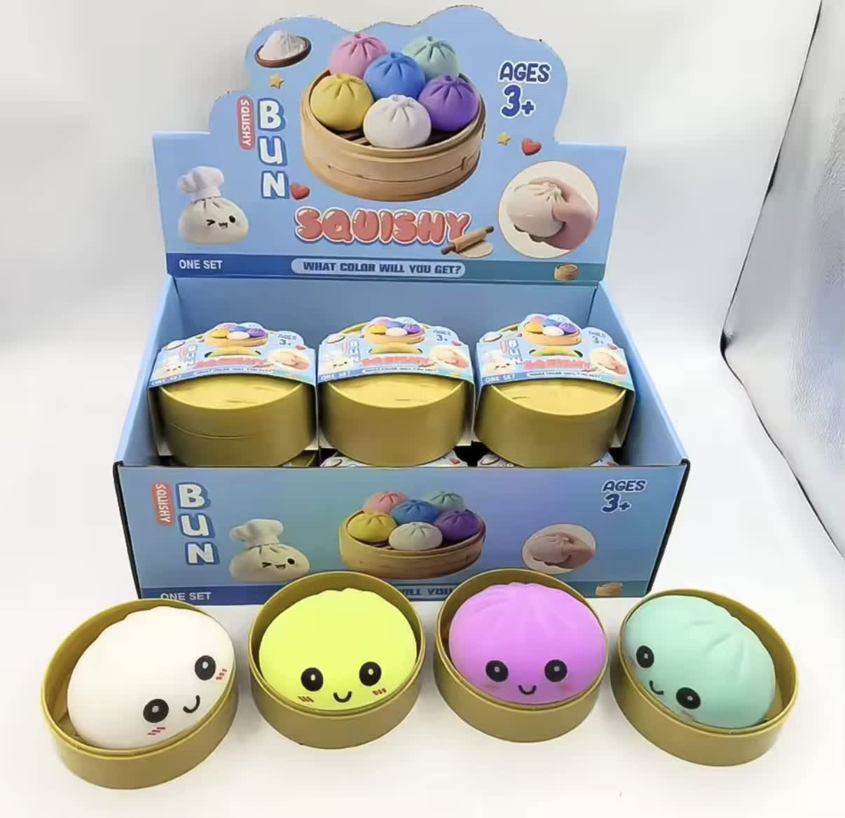 Four colorful squishy toys in round tins with a display box behind them