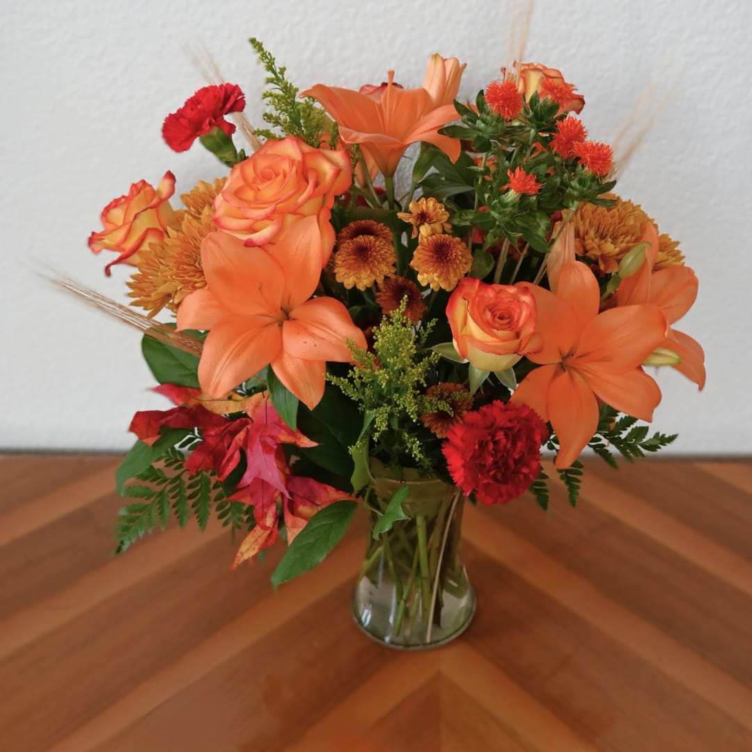 Orange and red mixed flower arrangement in a clear glass vase