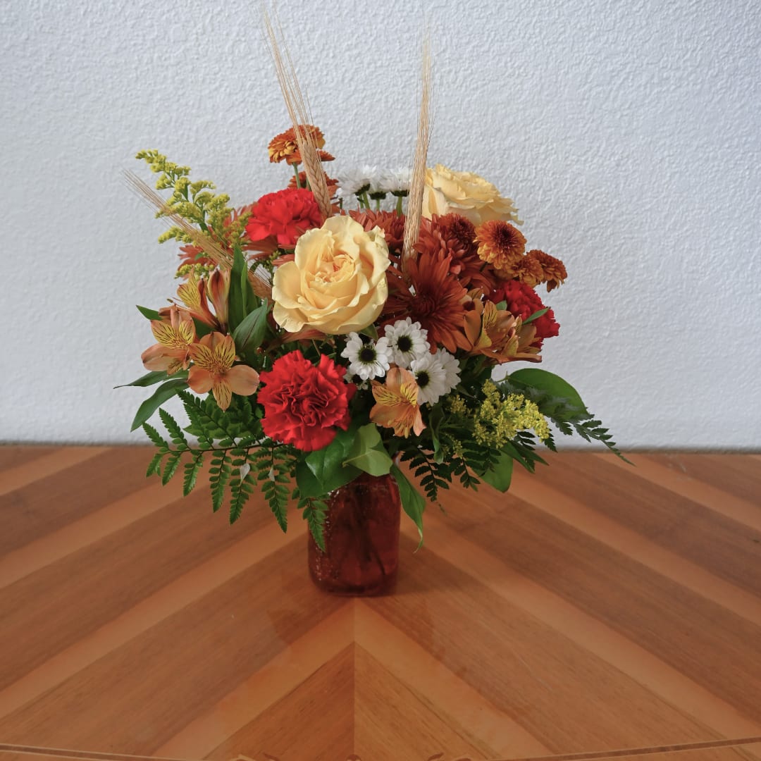 Mixed bouquet in a red glass vase with roses, carnations, and daisies