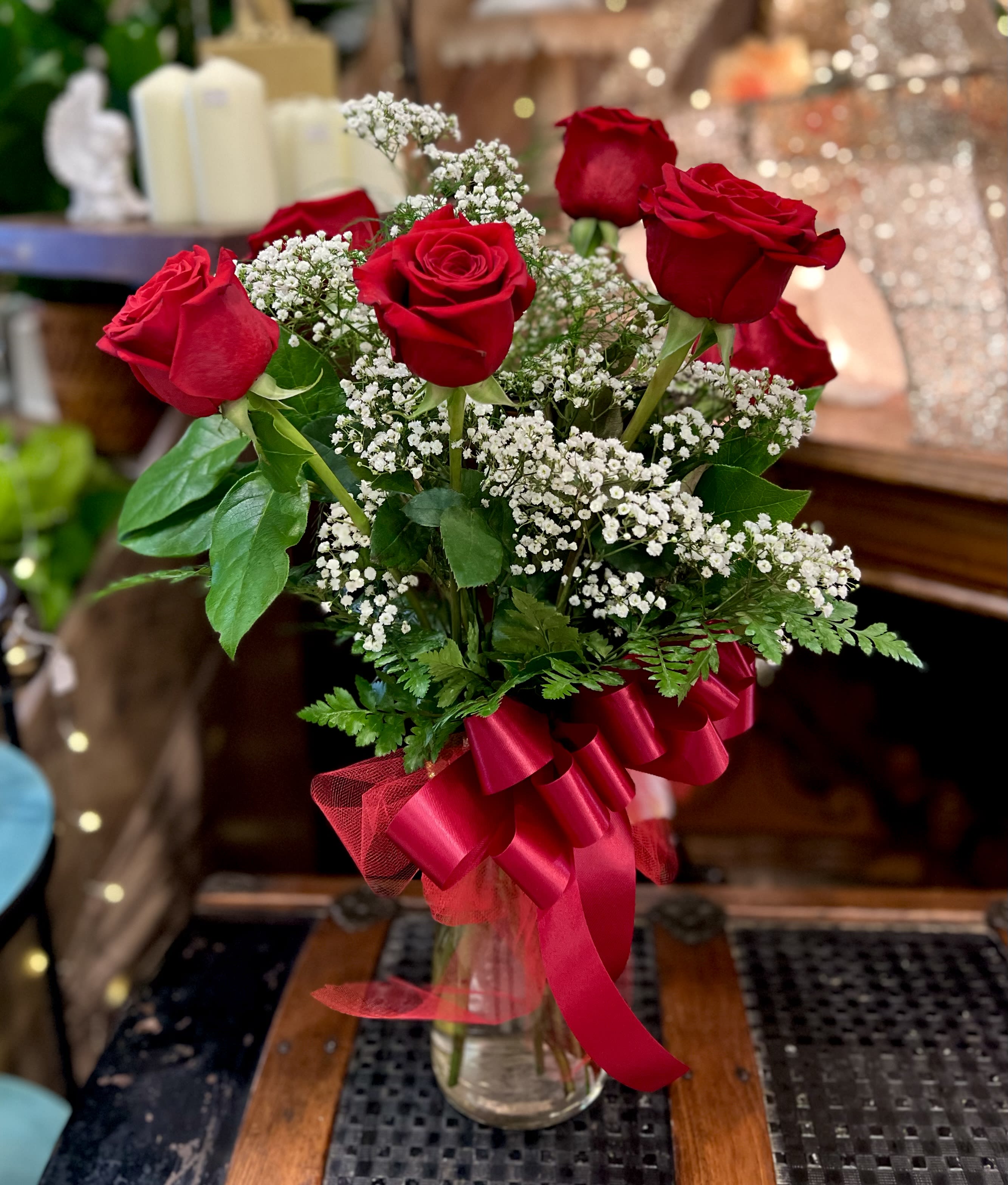 Red roses arranged in a glass vase with white baby's breath and a red ribbon.