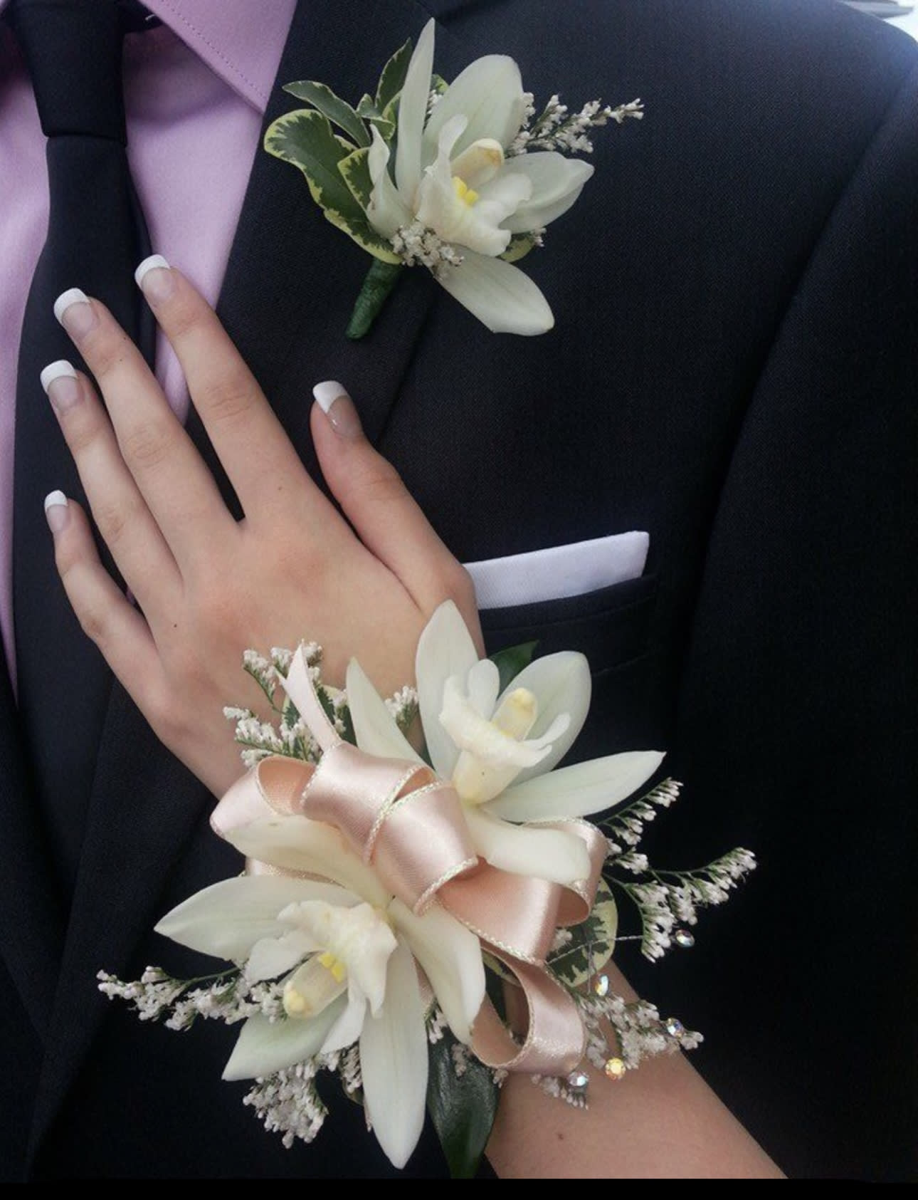 White floral corsage and boutonniere on a black suit with pink ribbon