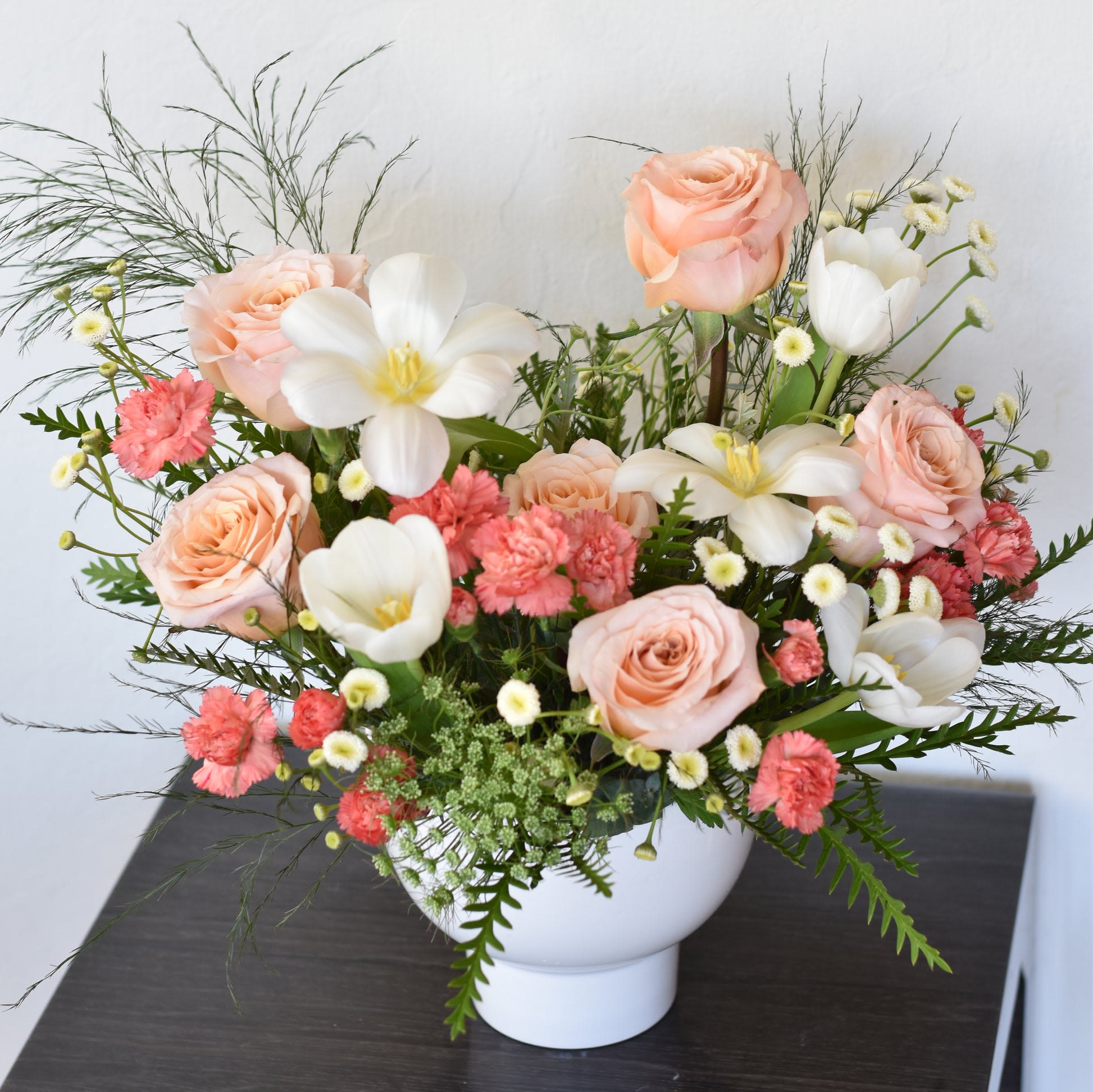 Sweet Love - The arrangement features a delicate blend of pristine white tulips and soft peachy roses, creating a harmonious symphony of elegance and warmth.  The white tulips, with their graceful, slender stems and pure petals, exude purity and innocence. Each bloom seems to dance with the gentlest breeze, radiating a sense of tranquility and serenity.  Complementing the tulips are the peachy roses, their tender petals unfurling like whispers of dawn. Their subtle hue evokes feelings of tenderness and affection, adding a touch of softness to the arrangement.  Together, these flowers create a captivating tableau, where purity meets warmth, and tranquility intertwines with affection. Whether adorning a tabletop or gracing a special occasion, this arrangement is sure to captivate hearts and inspire awe with its timeless beauty.