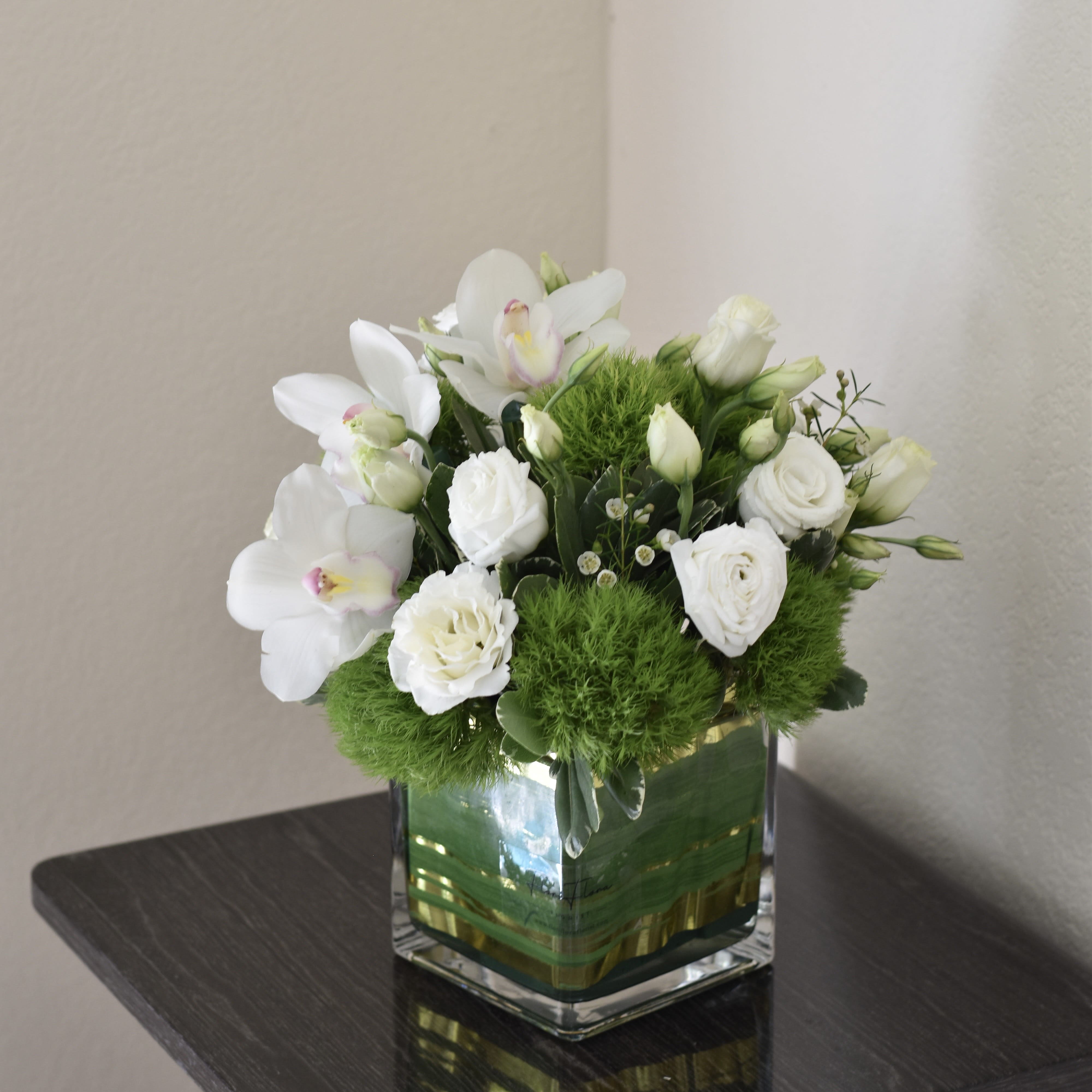 Something Grace... - "Something Grace" is an elegant and timeless flower arrangement that radiates pure sophistication and gentle beauty. This arrangement features pristine white Cymbidium orchids, known for their large, graceful blooms and delicate allure. These orchids are complemented by soft white lisianthuses, whose ruffled petals add a touch of romantic charm.  To add a fresh, vibrant contrast, green pompons are interspersed throughout the arrangement, their cheerful, round blooms bringing a lively burst of color. The combination of the serene white flowers and the lively green pompons creates a harmonious balance, evoking a sense of grace and understated elegance.  "Something Grace" is perfect for occasions where you want to convey a message of purity, tranquility, and timeless beauty.