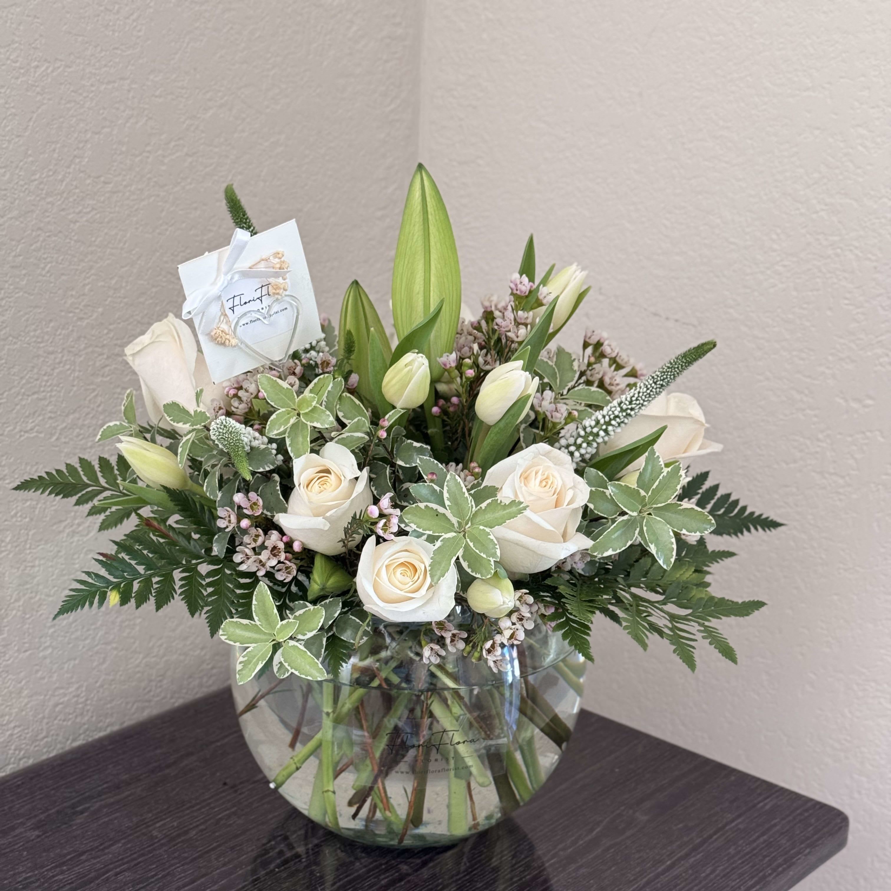 Peaceful Remembrance Bouquet - The "Peaceful Remembrance Bouquet" is a serene and elegant arrangement designed to convey heartfelt condolences and offer solace during times of grief.  At its core, delicate white tulips stand tall, symbolizing purity and new beginnings, their graceful petals gently unfurling. Nestled among them, pristine white roses exude a sense of innocence and reverence, their soft fragrance offering comfort and reassurance.  Interwoven within the arrangement, fragrant white lilies impart a sense of tranquility and eternal peace, their blossoms unfolding with quiet grace. Completing the ensemble, intricate white ranunculus blooms add a touch of delicate beauty, symbolizing charm and appreciation.  Together, these pristine blooms create a poignant display, evoking memories of cherished moments and offering a source of comfort and strength during difficult times. The "Peaceful Remembrance Bouquet" serves as a heartfelt tribute, honoring the life and legacy of a loved one with grace and dignity.