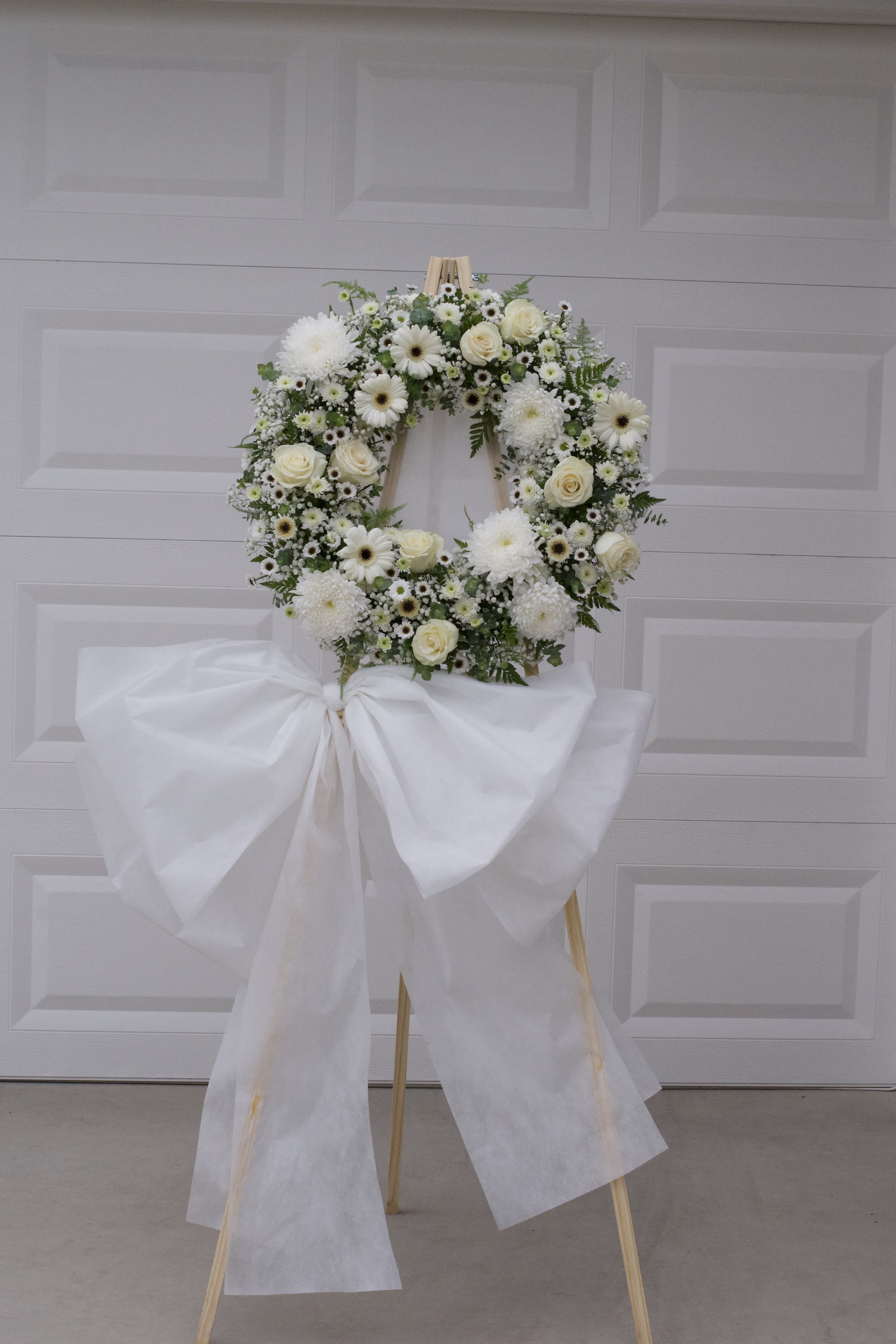 White floral wreath on a wooden easel with a large white bow