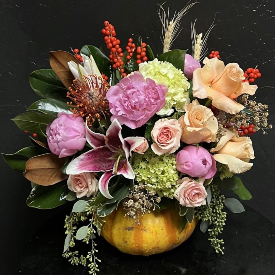 Mixed floral arrangement in a pumpkin-shaped container with pink, peach, and green blooms