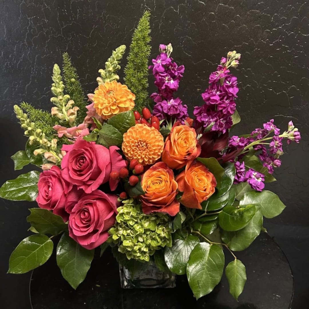 Pink and orange roses with purple flowers in a glass vase