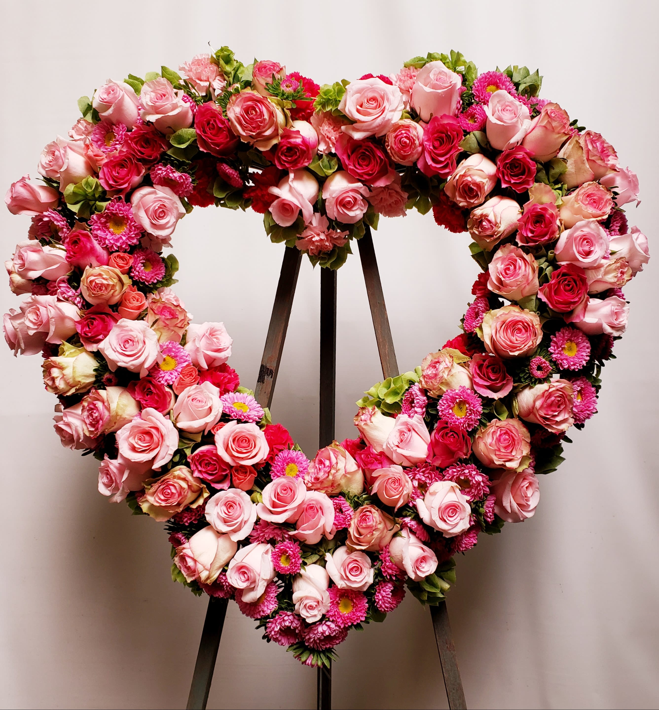 Heart-shaped floral wreath of pink roses and magenta blooms on a stand
