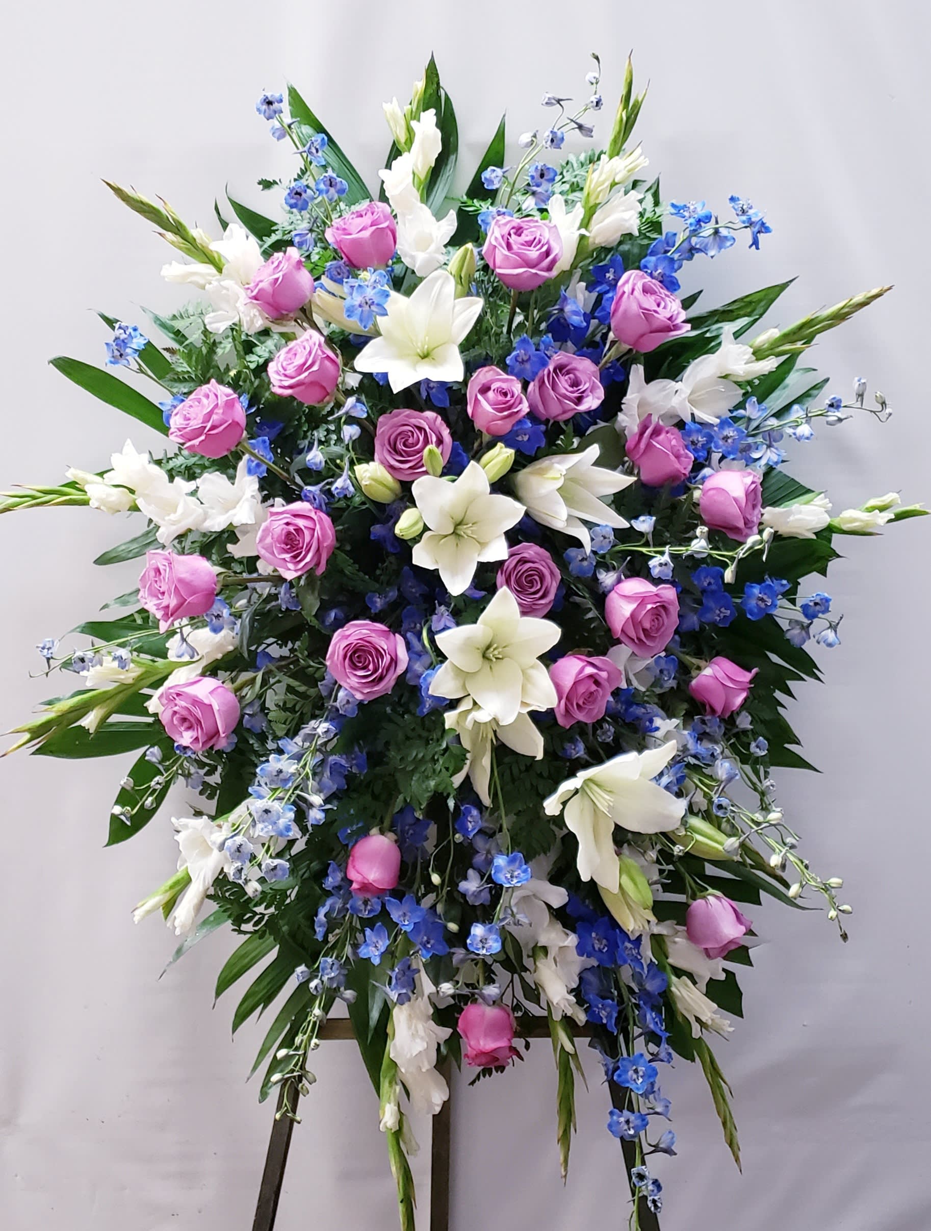 Large standing spray of pink roses, white lilies, and blue flowers