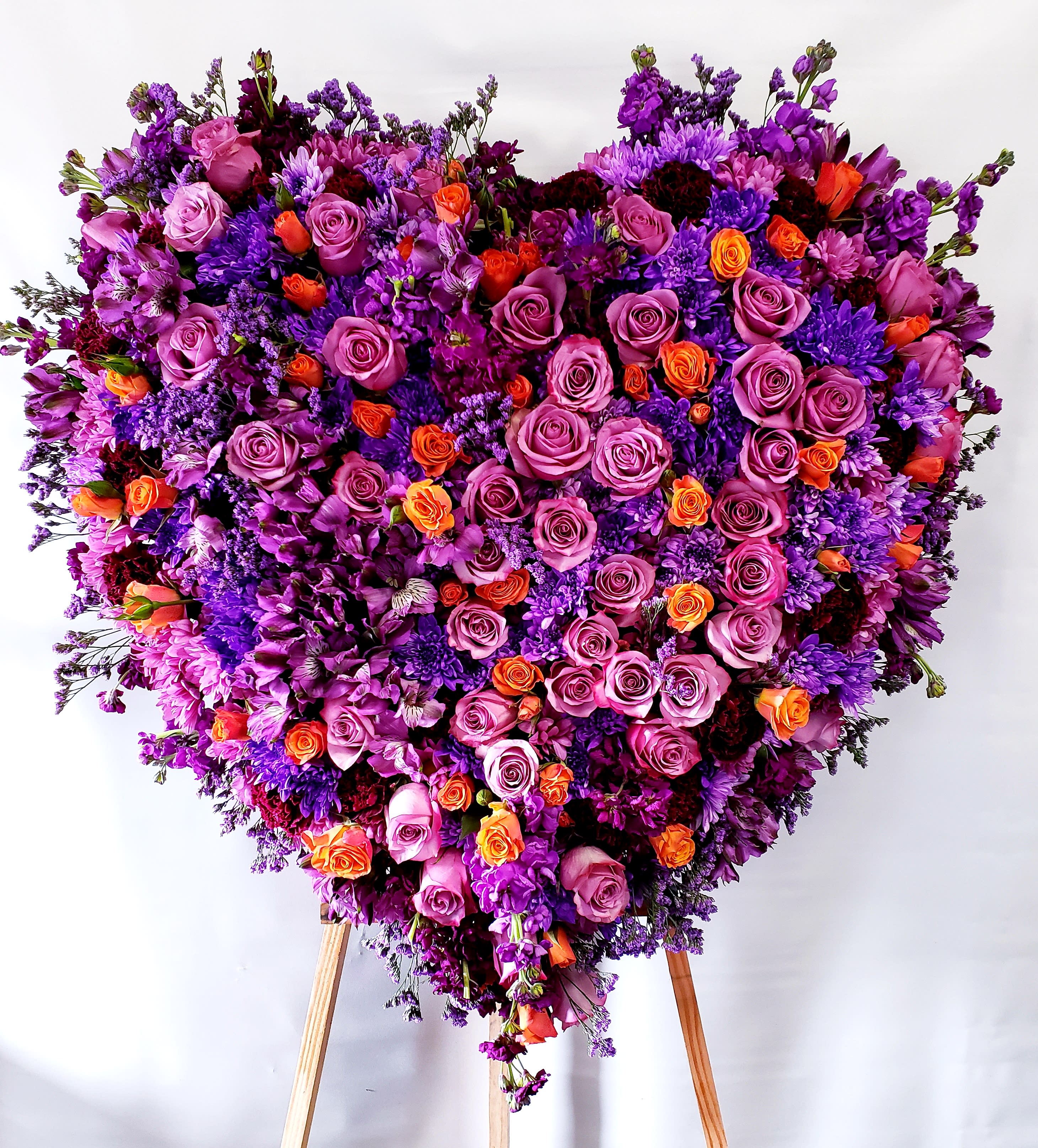 Large heart-shaped floral arrangement of purple, pink, and orange roses