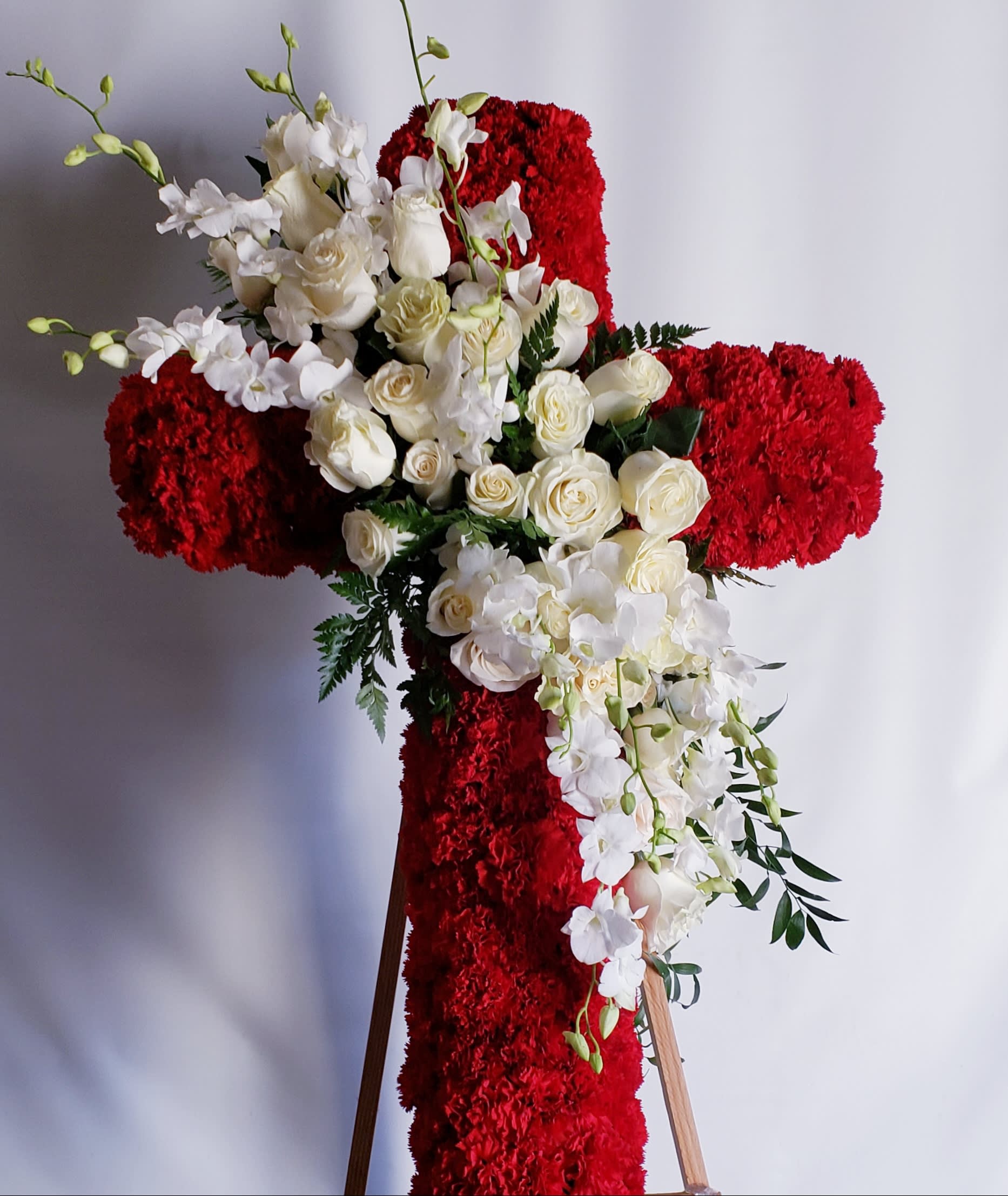 White roses and orchids arranged on a red floral cross