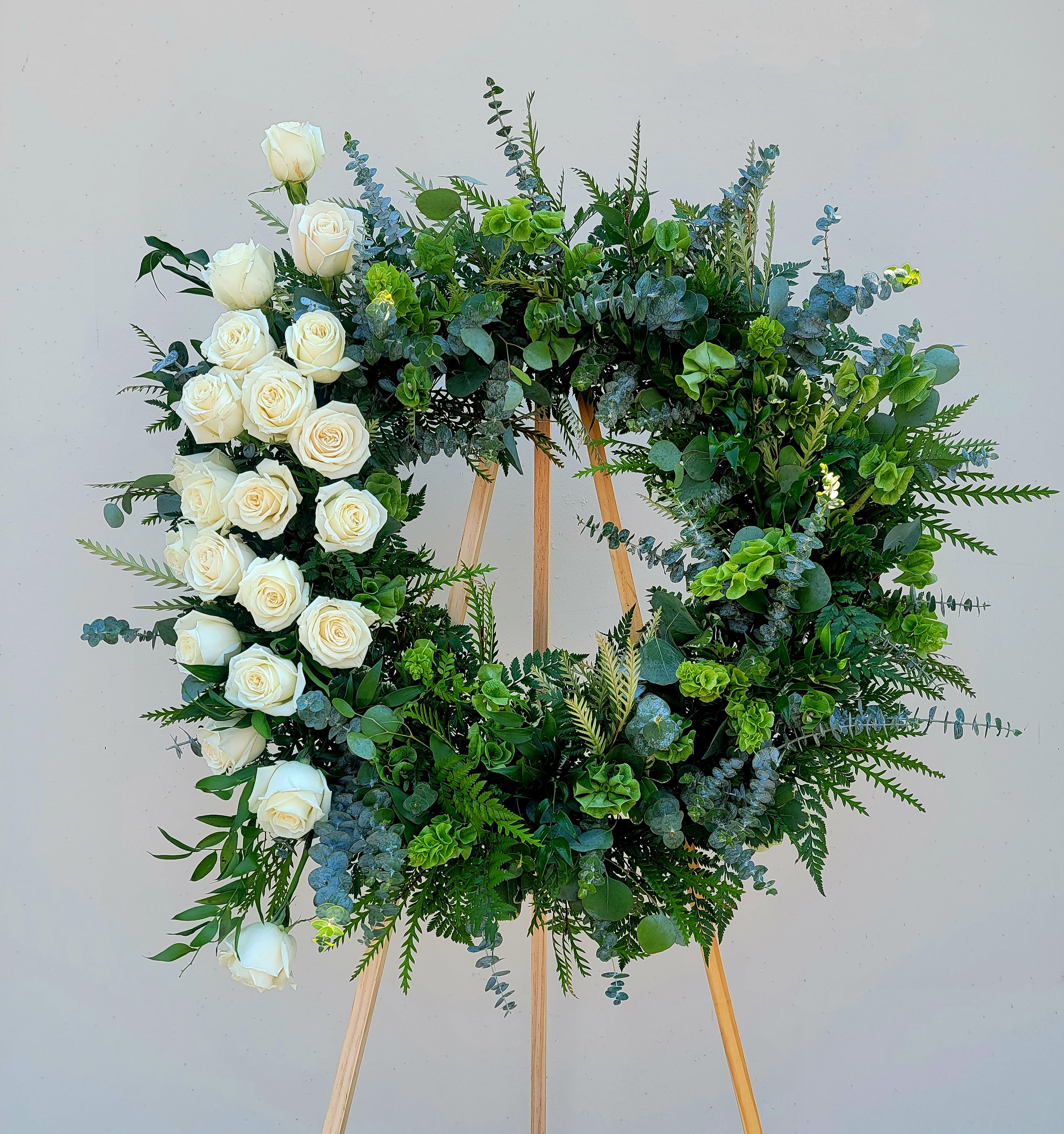 Circular floral wreath of white roses and mixed greenery on a wooden easel