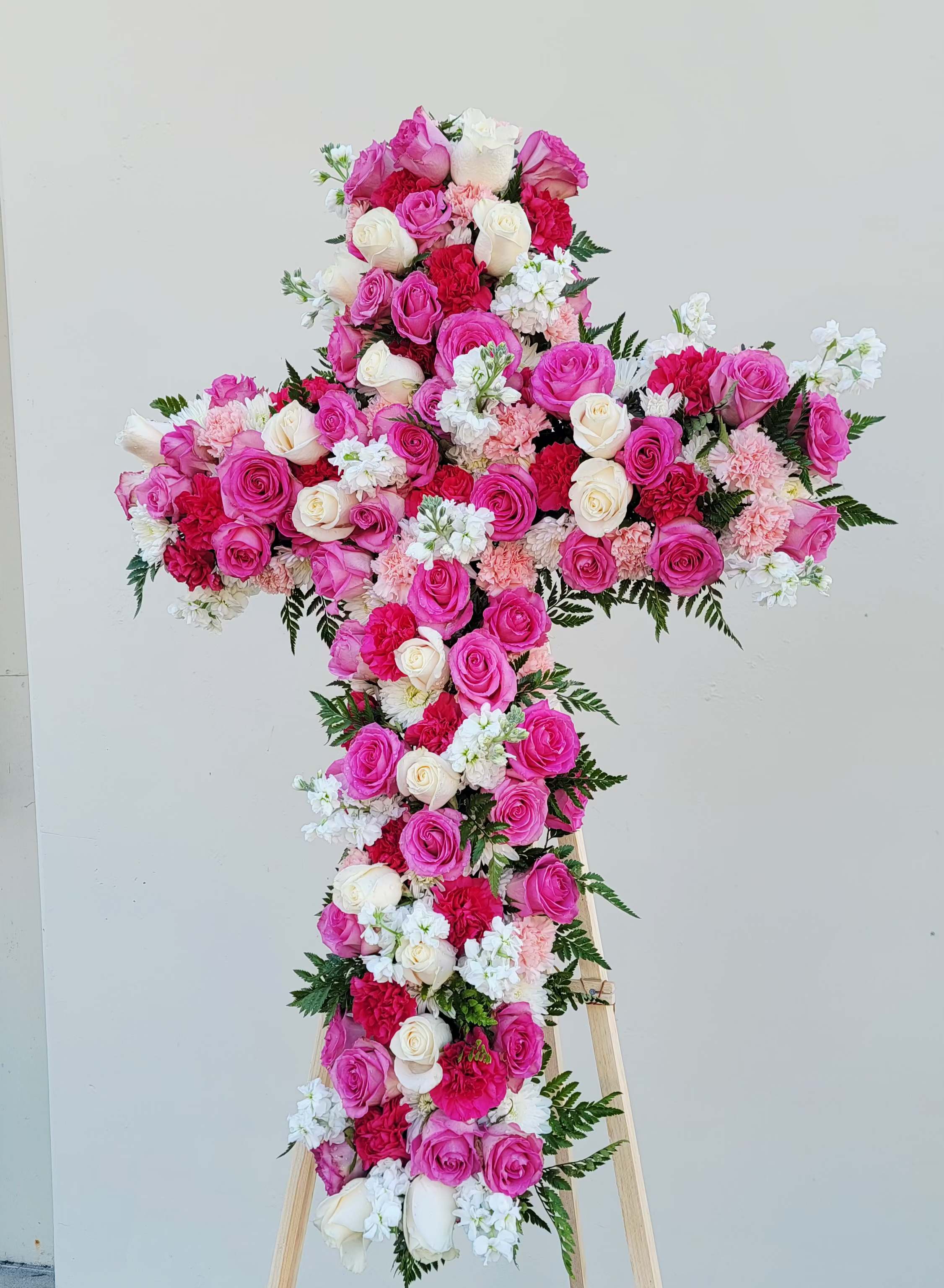 Cross-shaped floral arrangement of pink and white roses on a stand