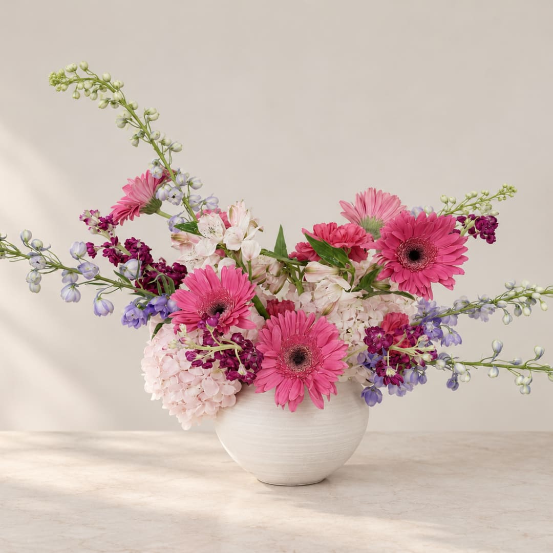 Pink gerbera daisies and mixed blooms in a white vase