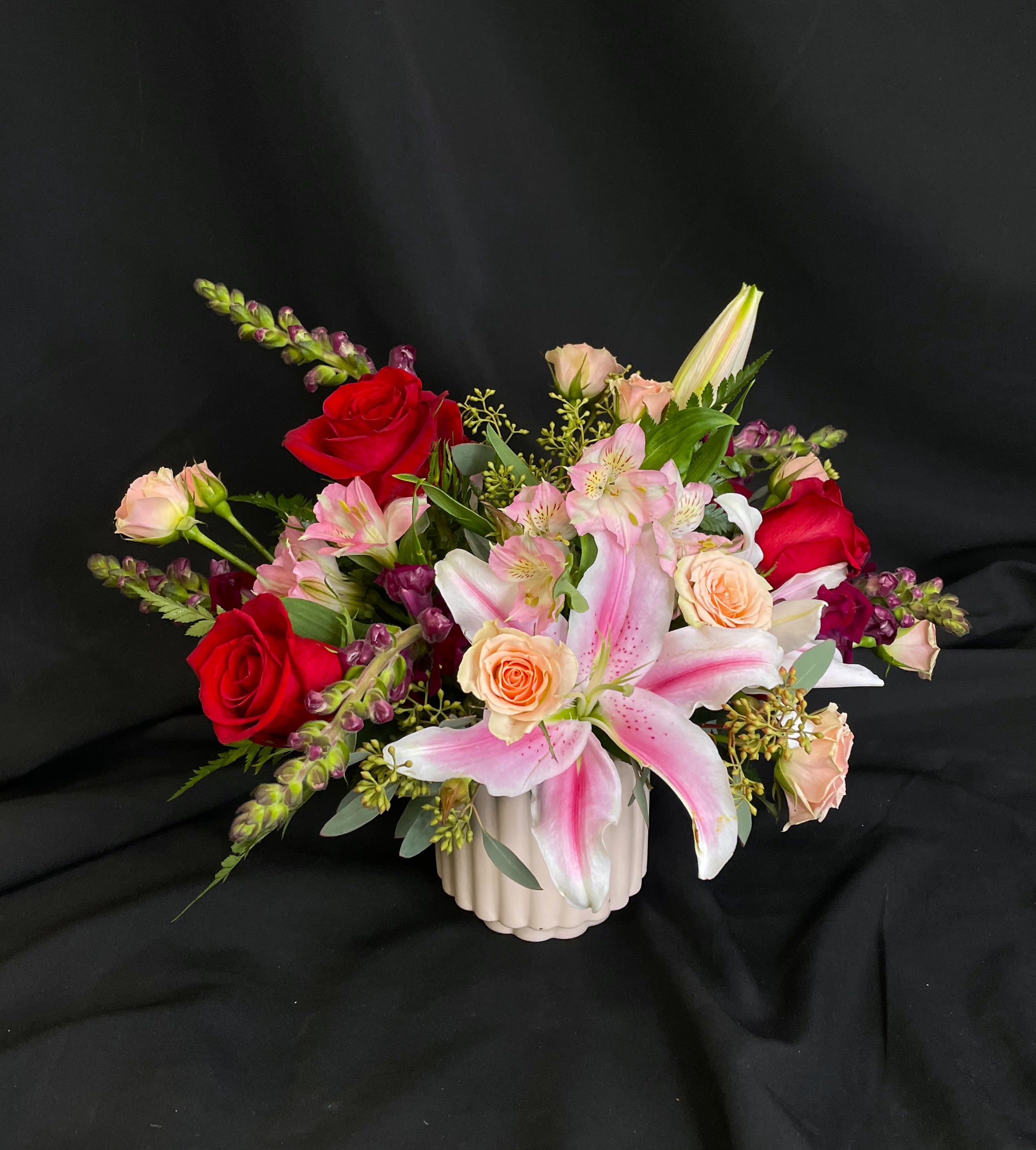 Mixed bouquet with pink lilies, red and peach roses in a white vase