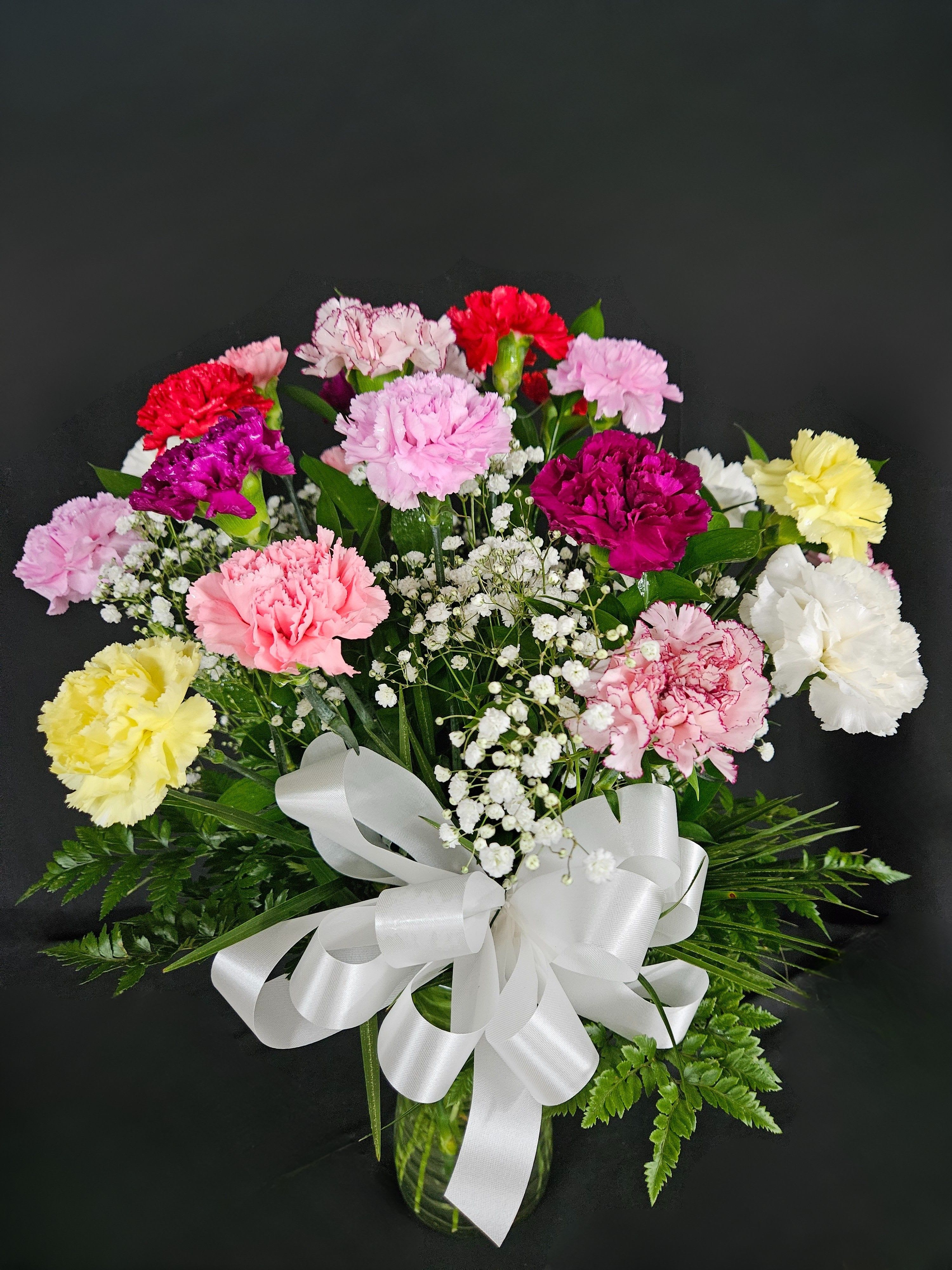 Bouquet of multicolored carnations in a glass vase with a white ribbon