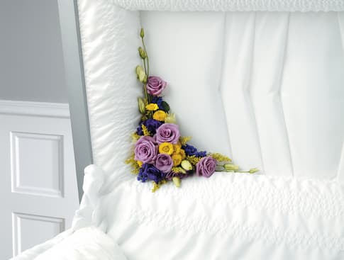 Purple and yellow floral spray arranged on a white casket