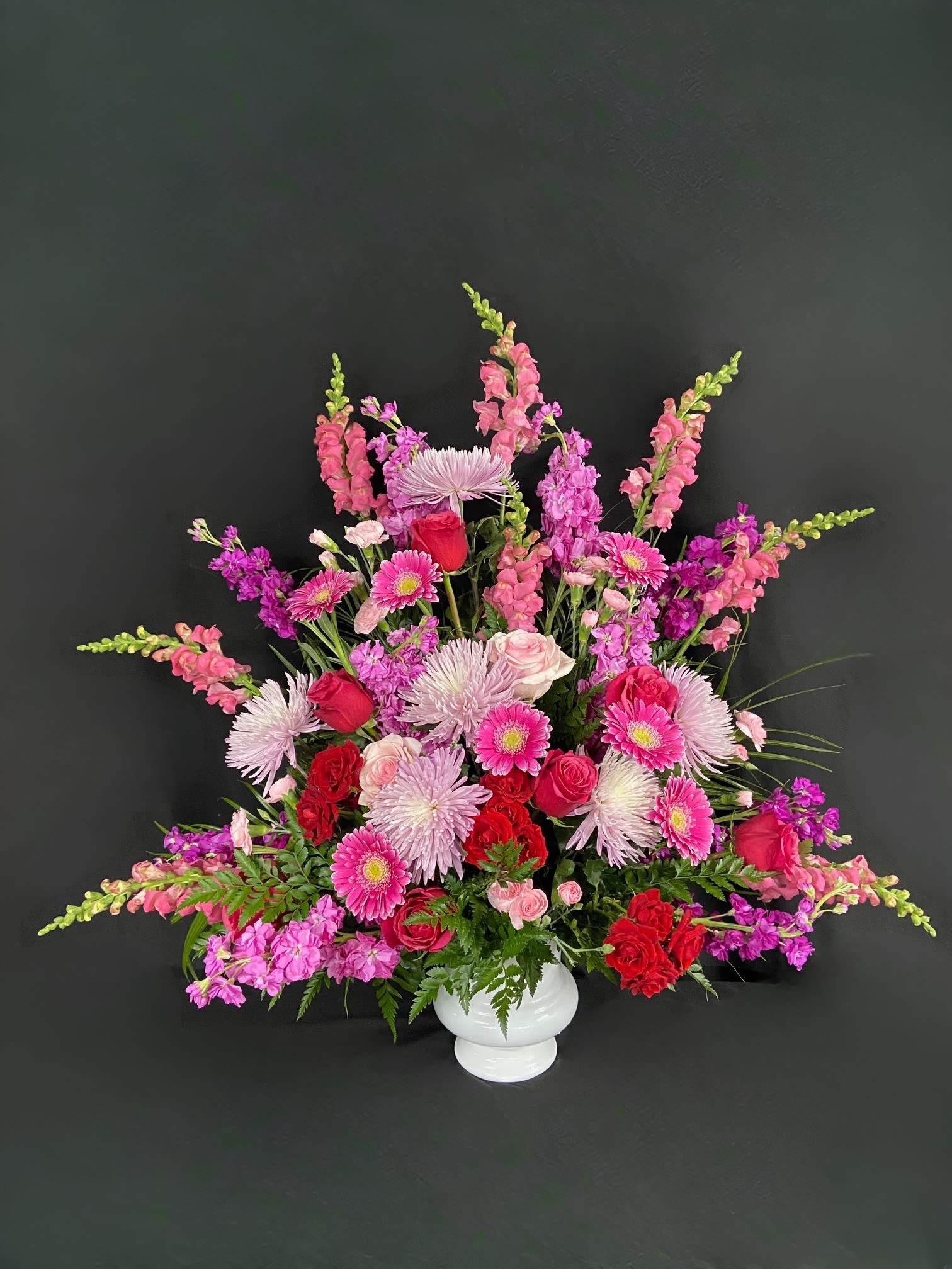 Large pink and red floral arrangement in a white vase