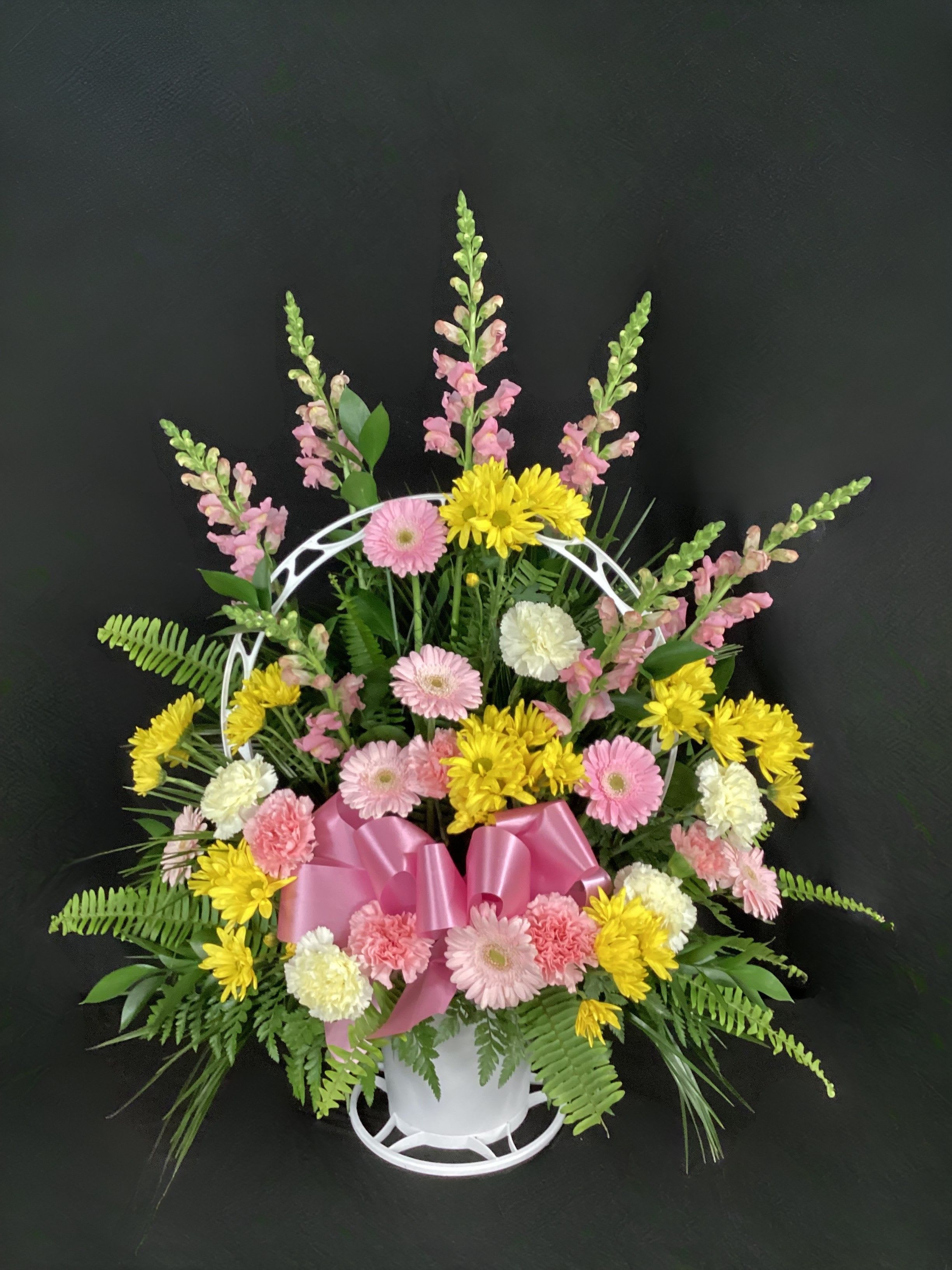 Pink and yellow mixed flower arrangement in a white basket with a pink bow