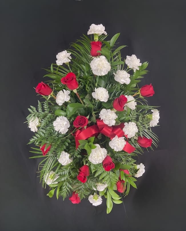 Red roses and white carnations in a standing spray with a red ribbon