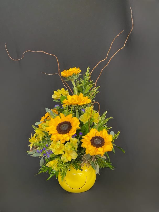 Sunflower arrangement in a yellow smiley-face vase with curly branches