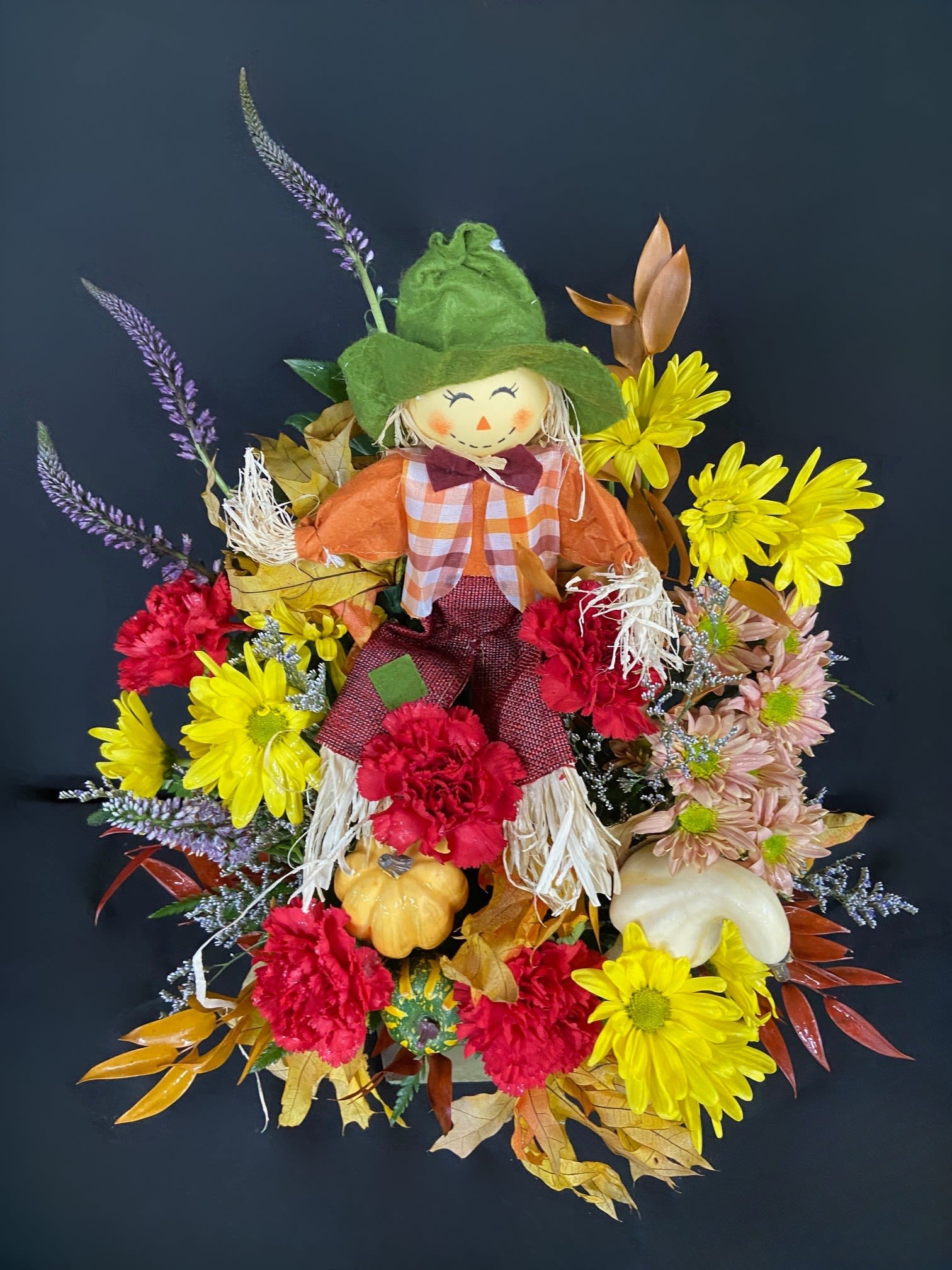 Scarecrow decoration surrounded by yellow, red, and pink flowers