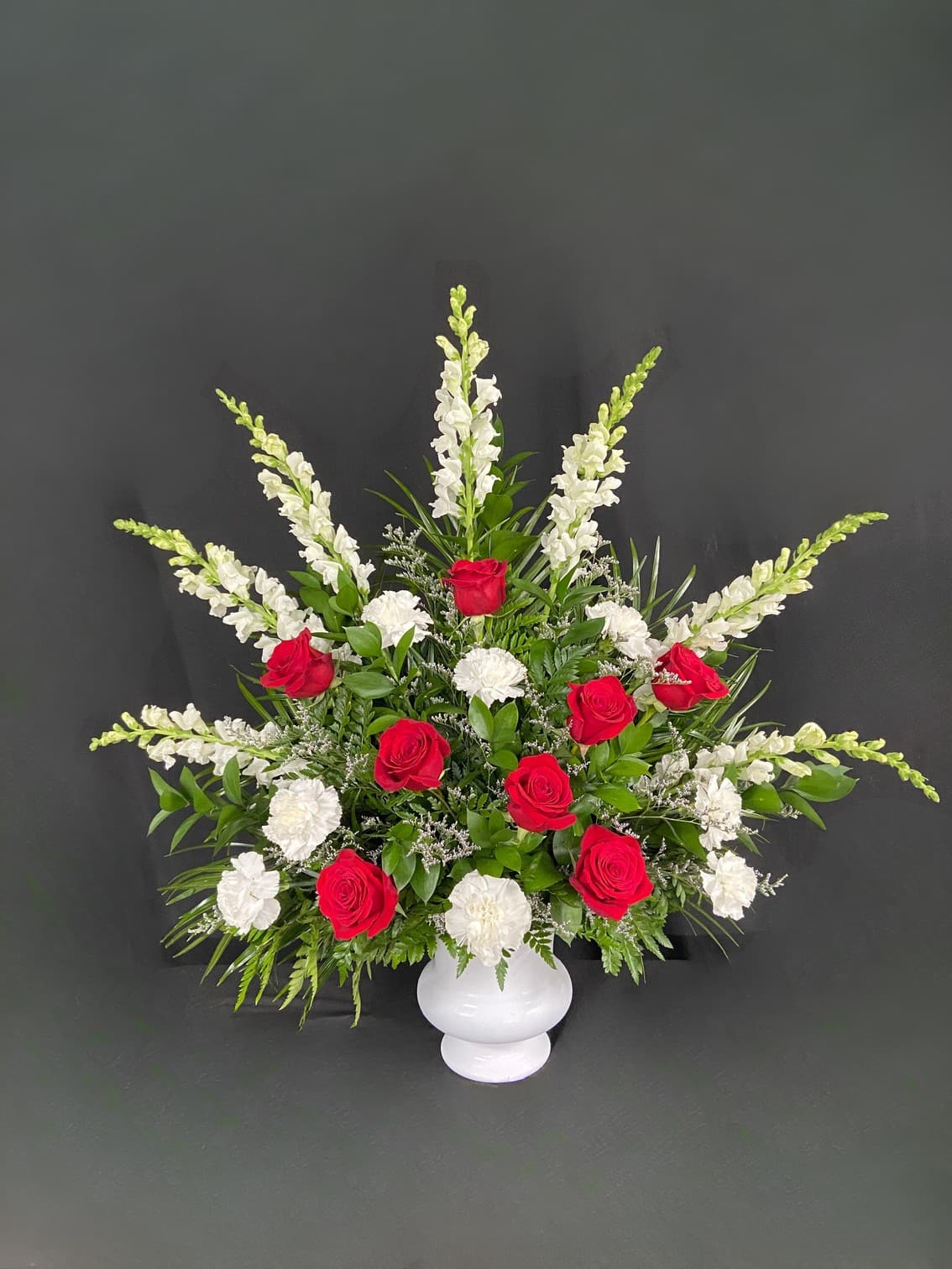Red roses and white flowers in a white vase with greenery