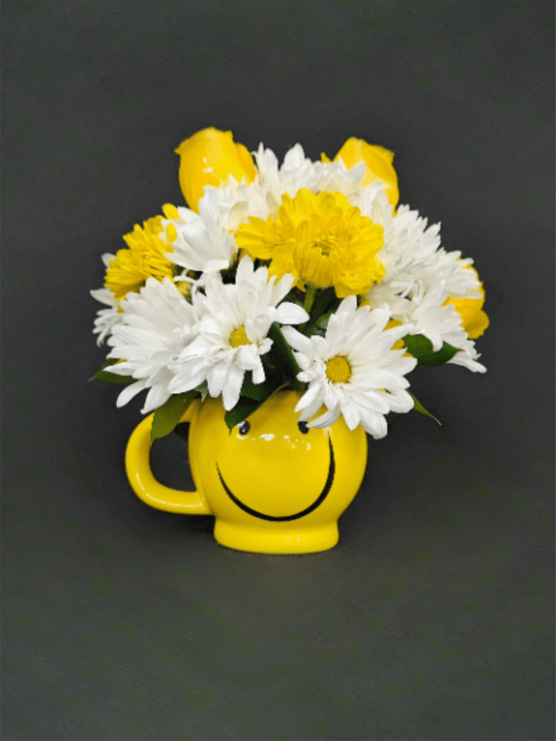 Yellow smiley-face mug filled with white daisies, yellow daisies, and yellow roses on a dark background