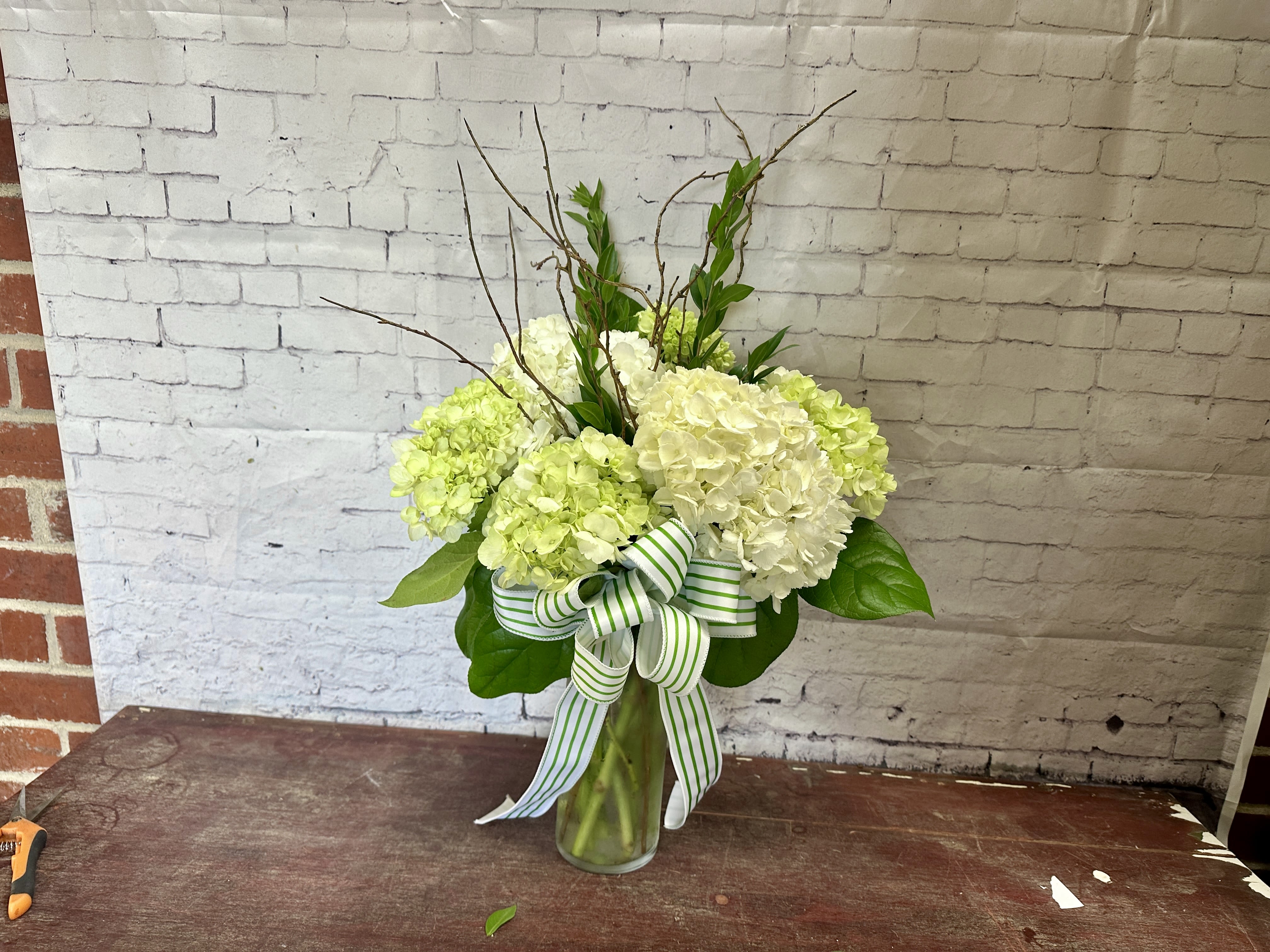 Twig and bloom  - Several large white and pale green hydrangea blooms in a clear glass vase with branches 