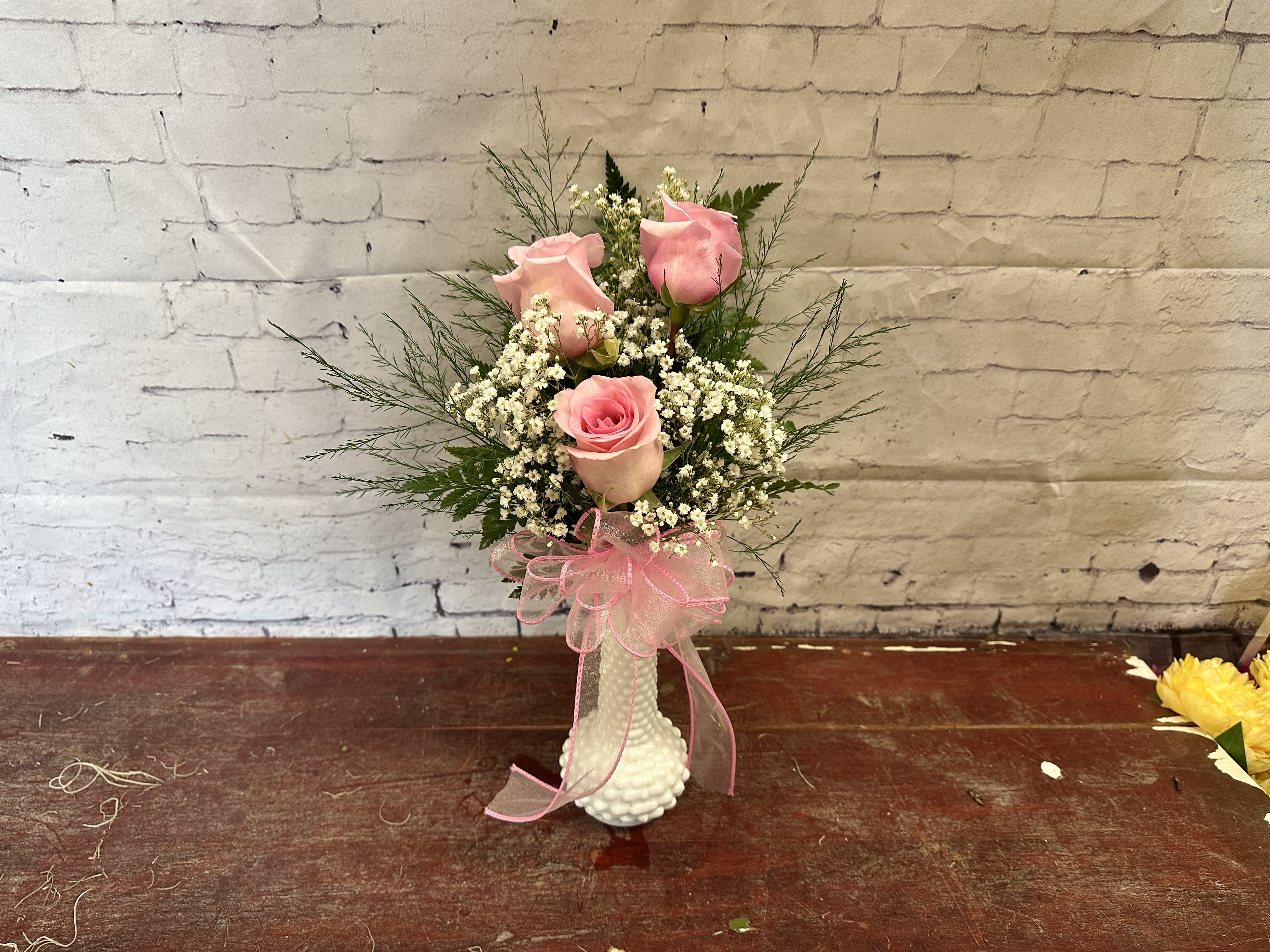 Pink roses in a white vase with a pink ribbon