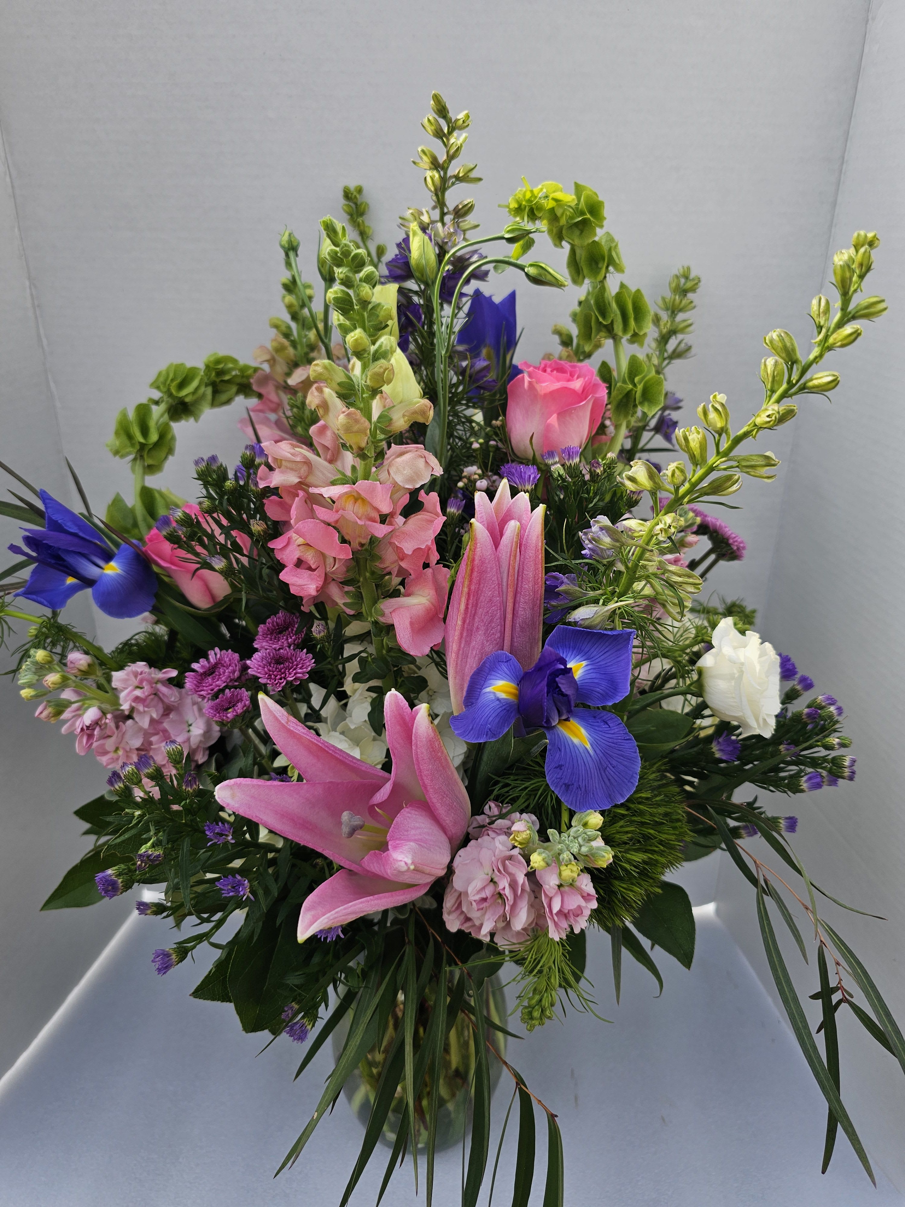 Mixed bouquet with pink lilies, blue irises, and pink roses in a glass vase