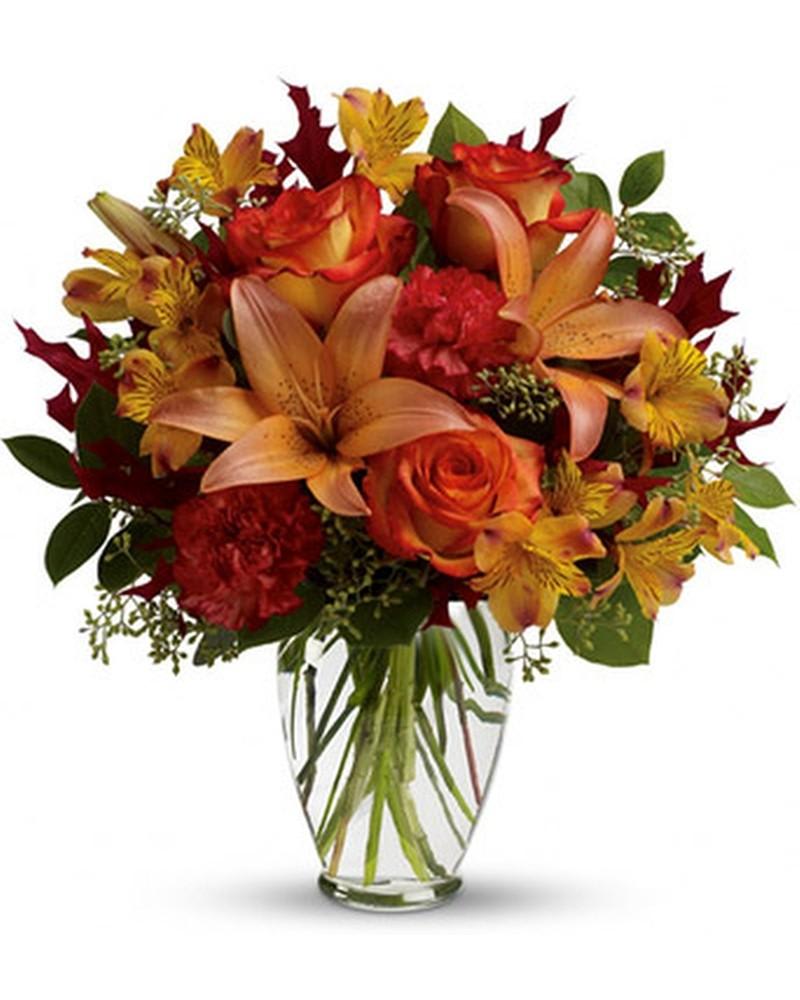 Orange roses and lilies in a clear glass vase with red and yellow accents
