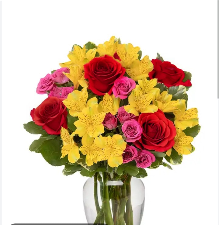 Bouquet of red roses, pink spray roses, and yellow flowers in a glass vase