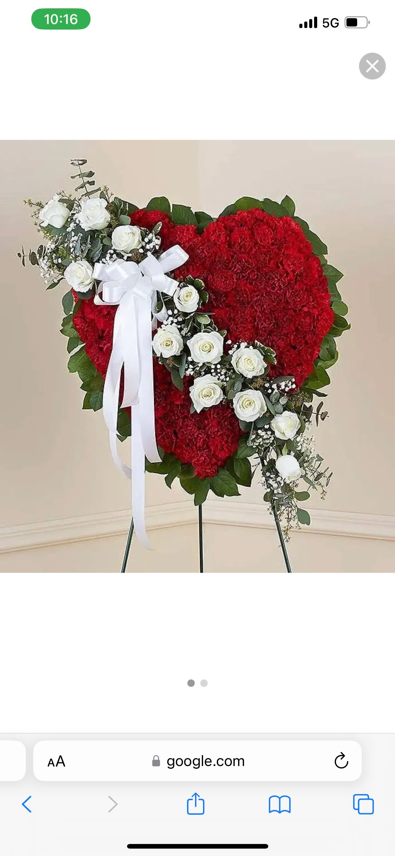 Standing heart-shaped spray of red carnations with white roses and a white ribbon on an easel.