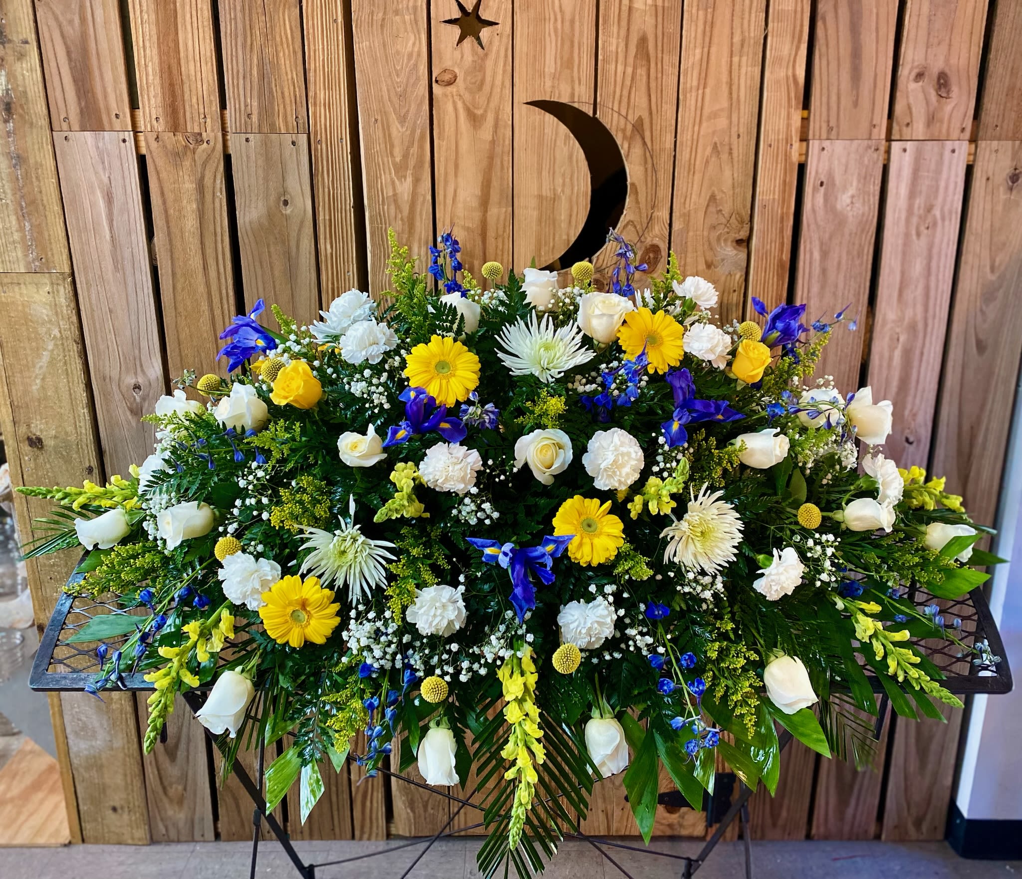 Large funeral spray with white, yellow, and blue flowers on a stand