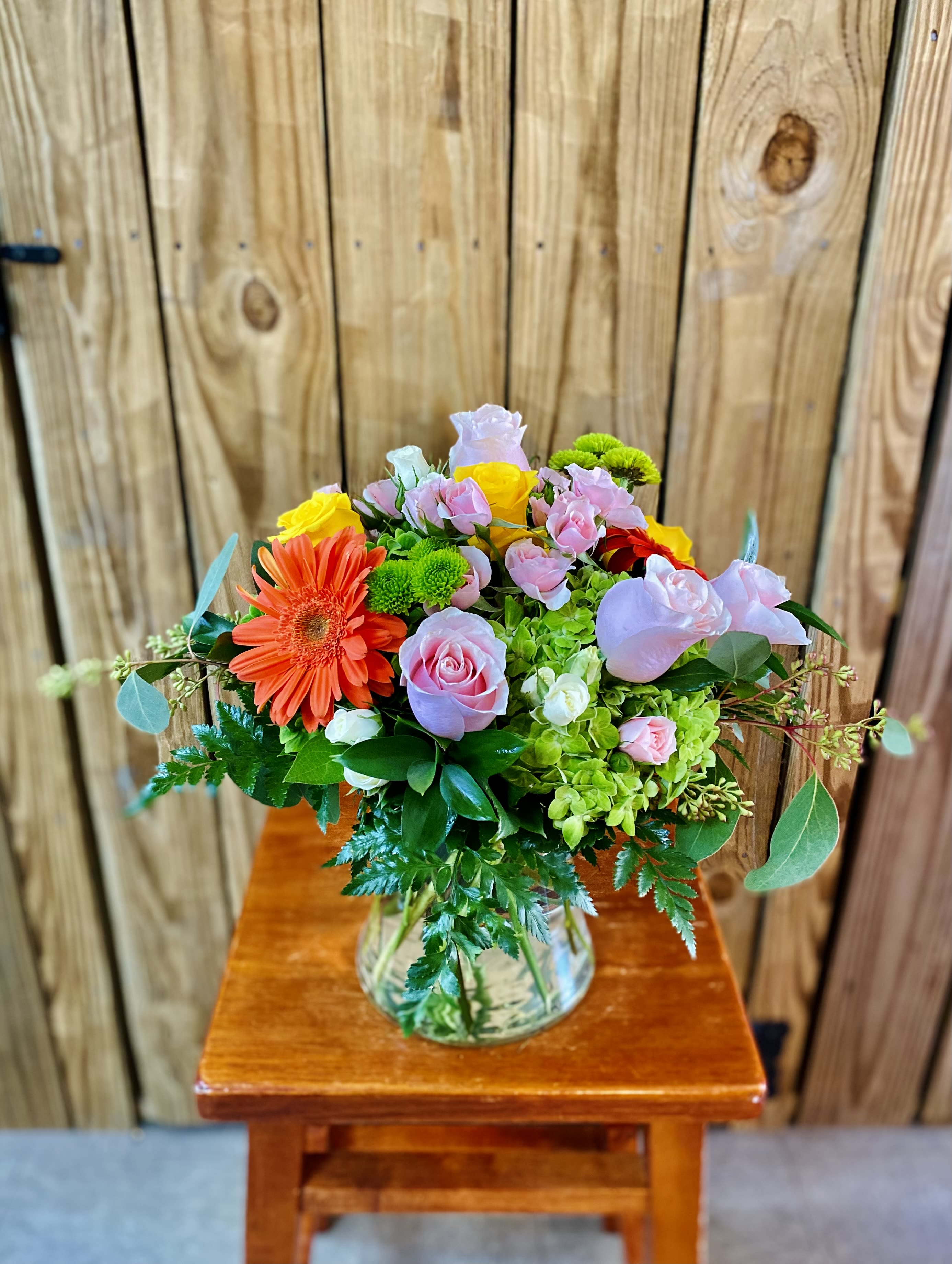 Mixed bouquet in a clear glass vase with pink roses and an orange gerbera daisy