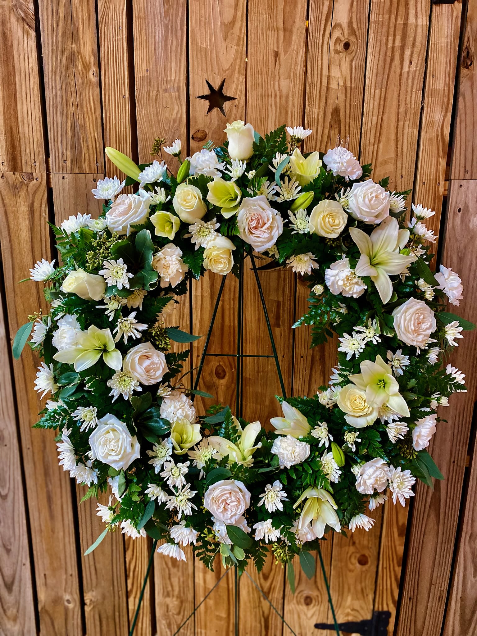 White floral wreath on a metal stand with roses and lilies