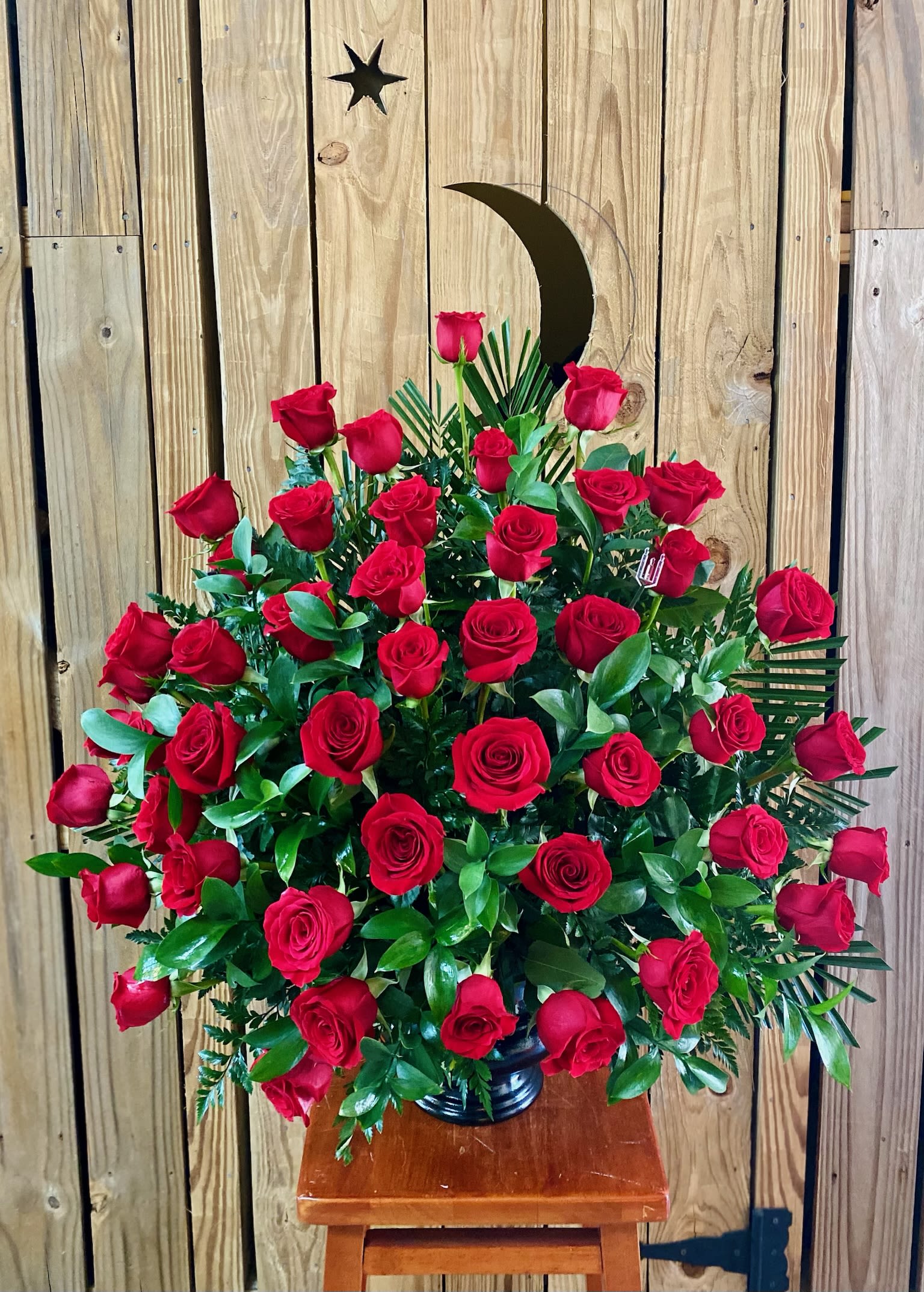 Large bouquet of red roses in a black vase with a crescent moon pick