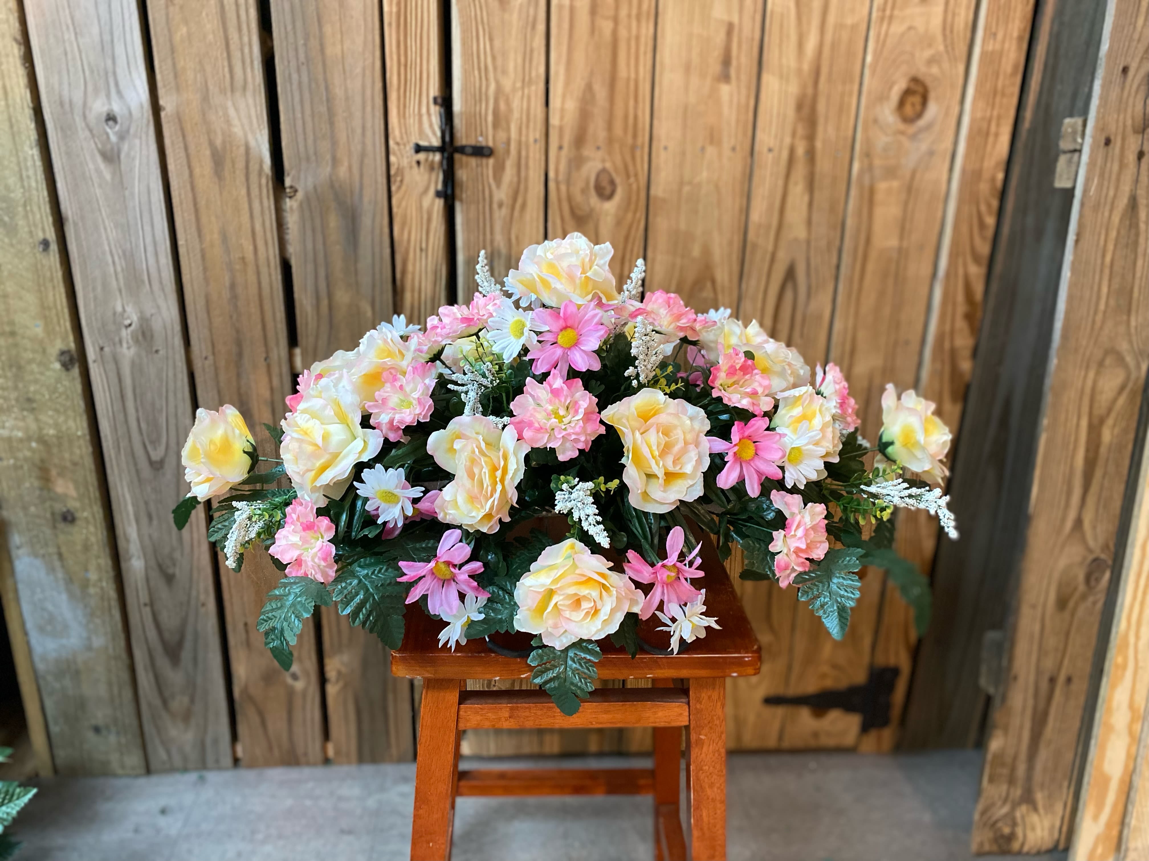 Low arrangement of yellow roses and pink daisies displayed on a wooden stool