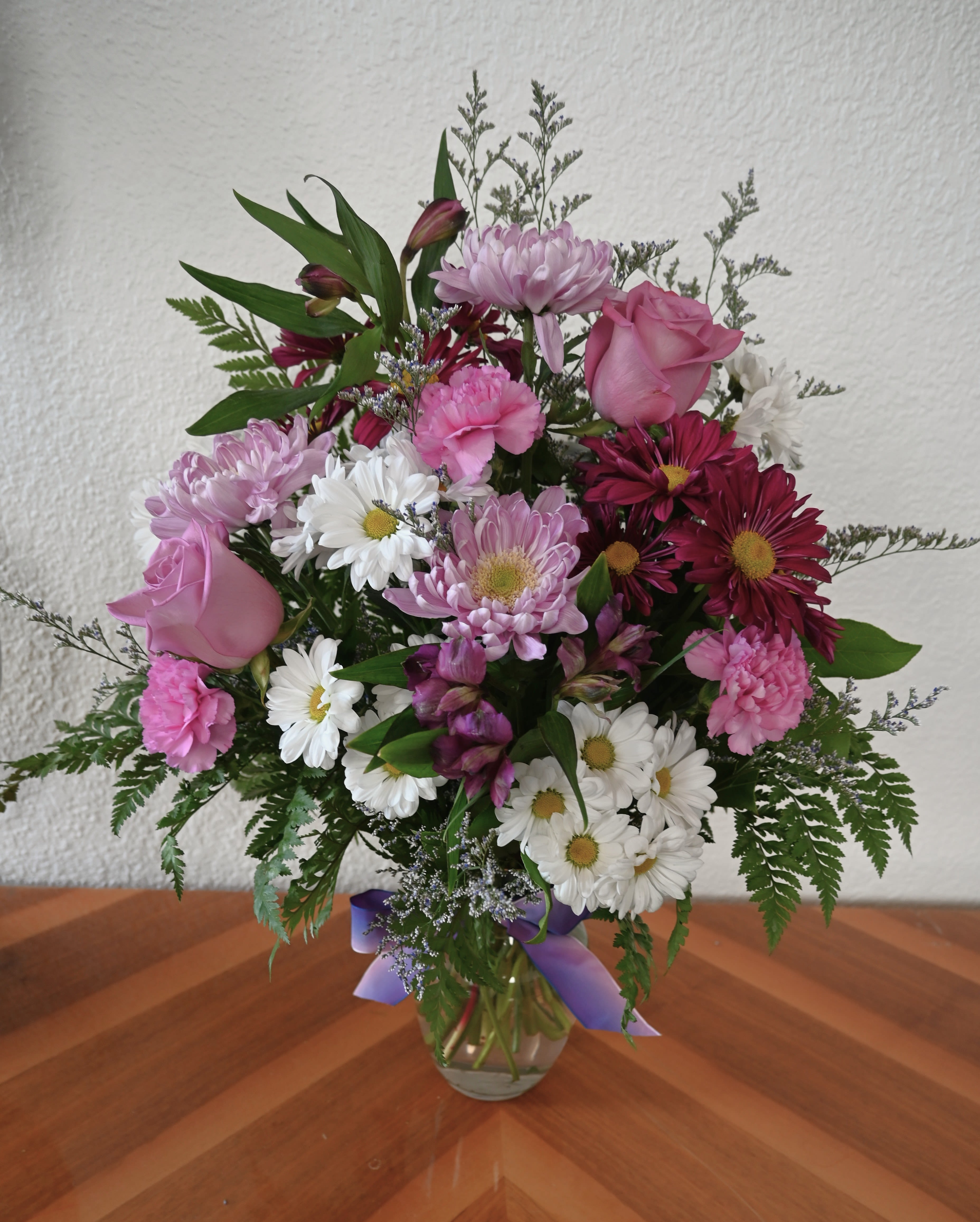 Mixed pink and white bouquet in a glass vase with a purple ribbon