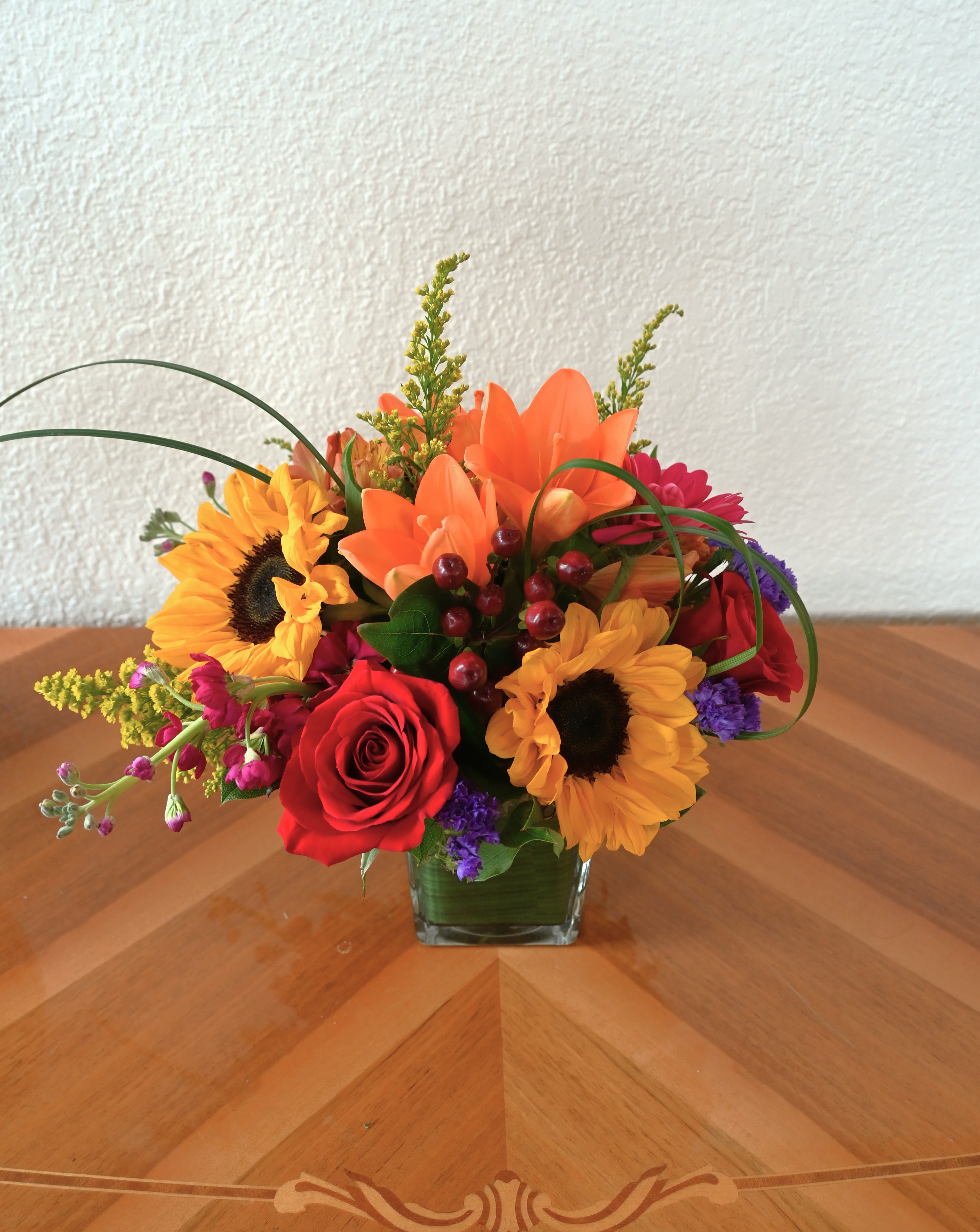 Garden Medley - Capture the charm of a stroll through the garden with this vibrant collection of radiant sunflowers, lush red roses, and elegant lilies. Each flower brings its own unique beauty to the arrangement, creating a beautiful display.