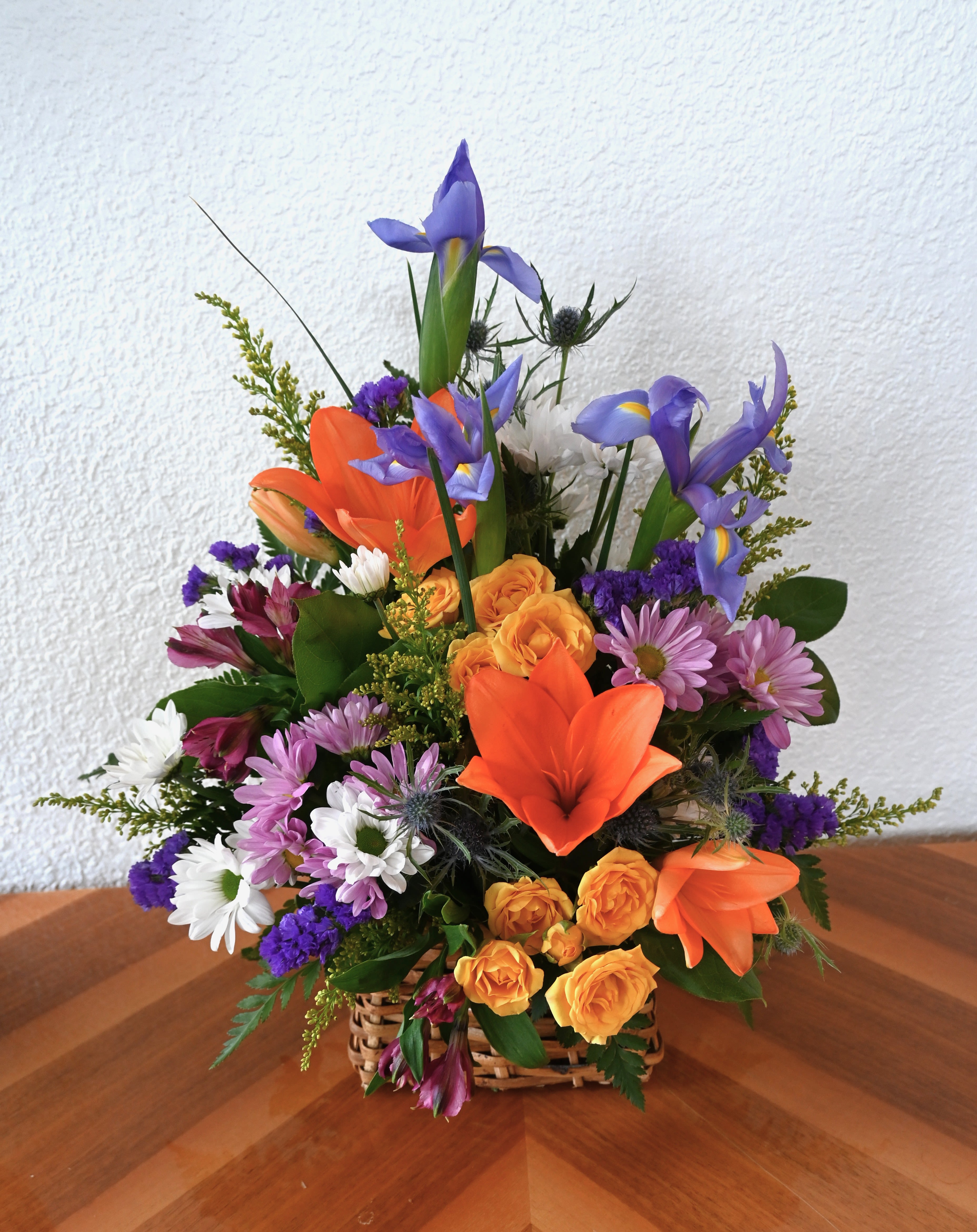 Basket of Joy - This playful tribute to spring features daisies, spray roses, lilies, iris, and alstroemeria. This beautiful arrangement captures the freshness and energy of spring, making it perfect for any celebration.  Ideal for any occasion, Basket of Joy brings a bright burst of spring to any space!
