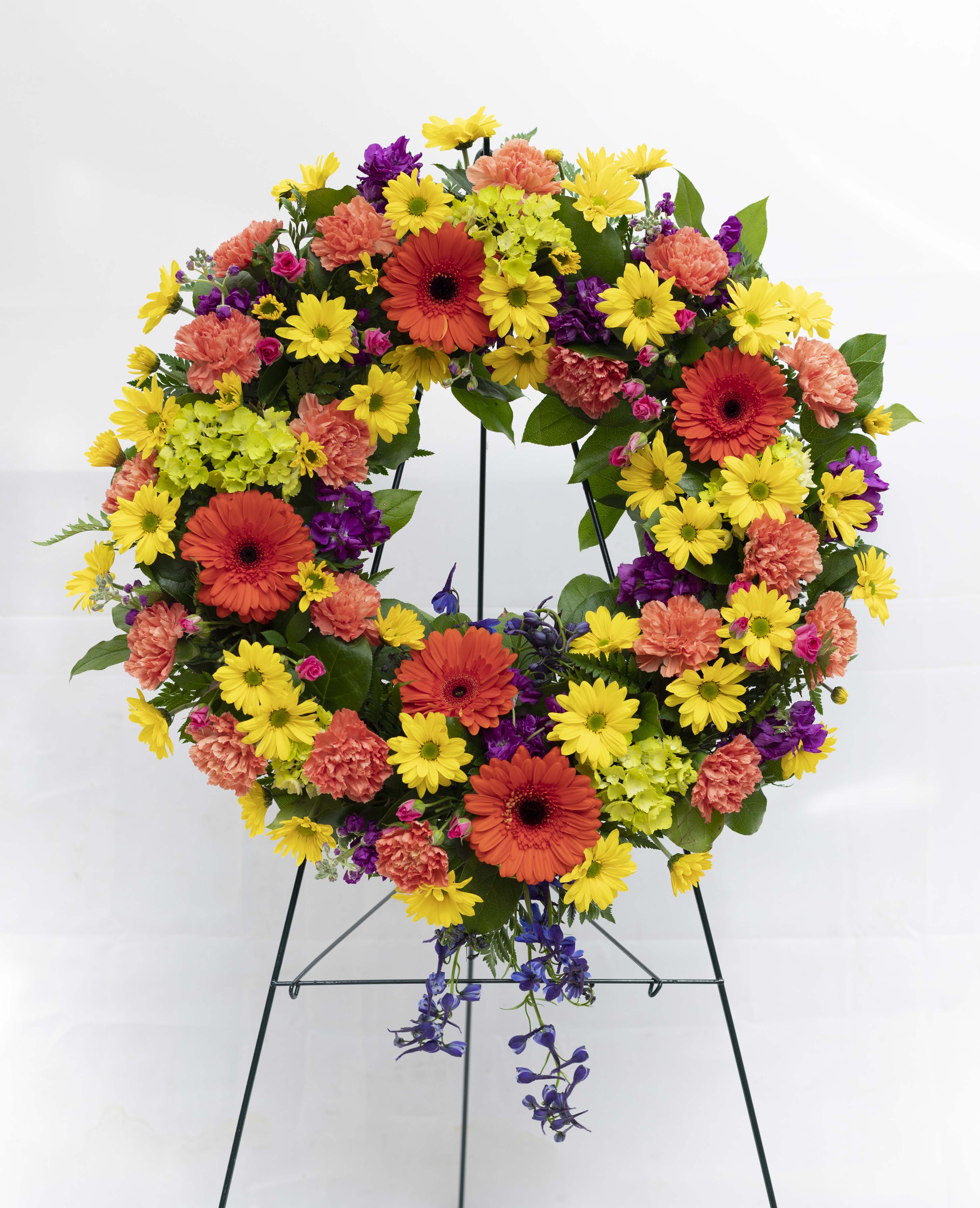 Colorful floral wreath on a metal stand with yellow, orange, purple, and pink blooms
