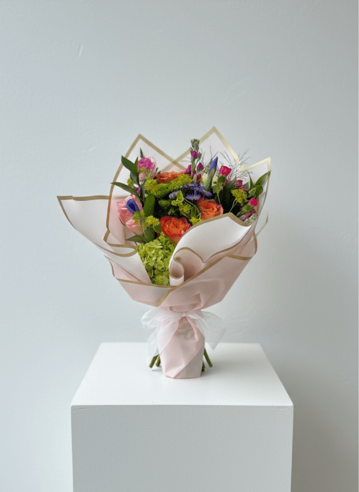 Bouquet of orange, pink, and purple flowers wrapped in pale pink paper
