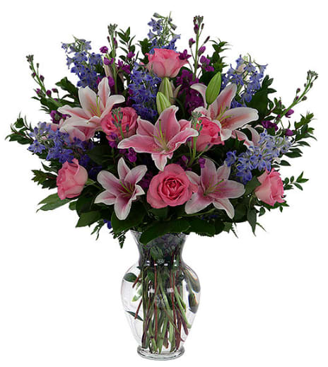 Pink lilies and roses with blue flowers in a clear glass vase
