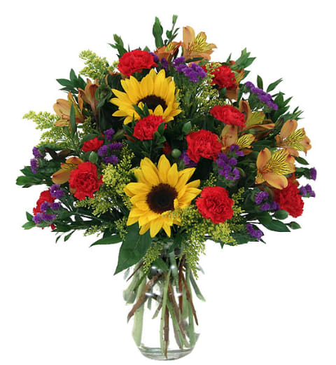 Bouquet of sunflowers, red carnations, and purple accents in a glass vase